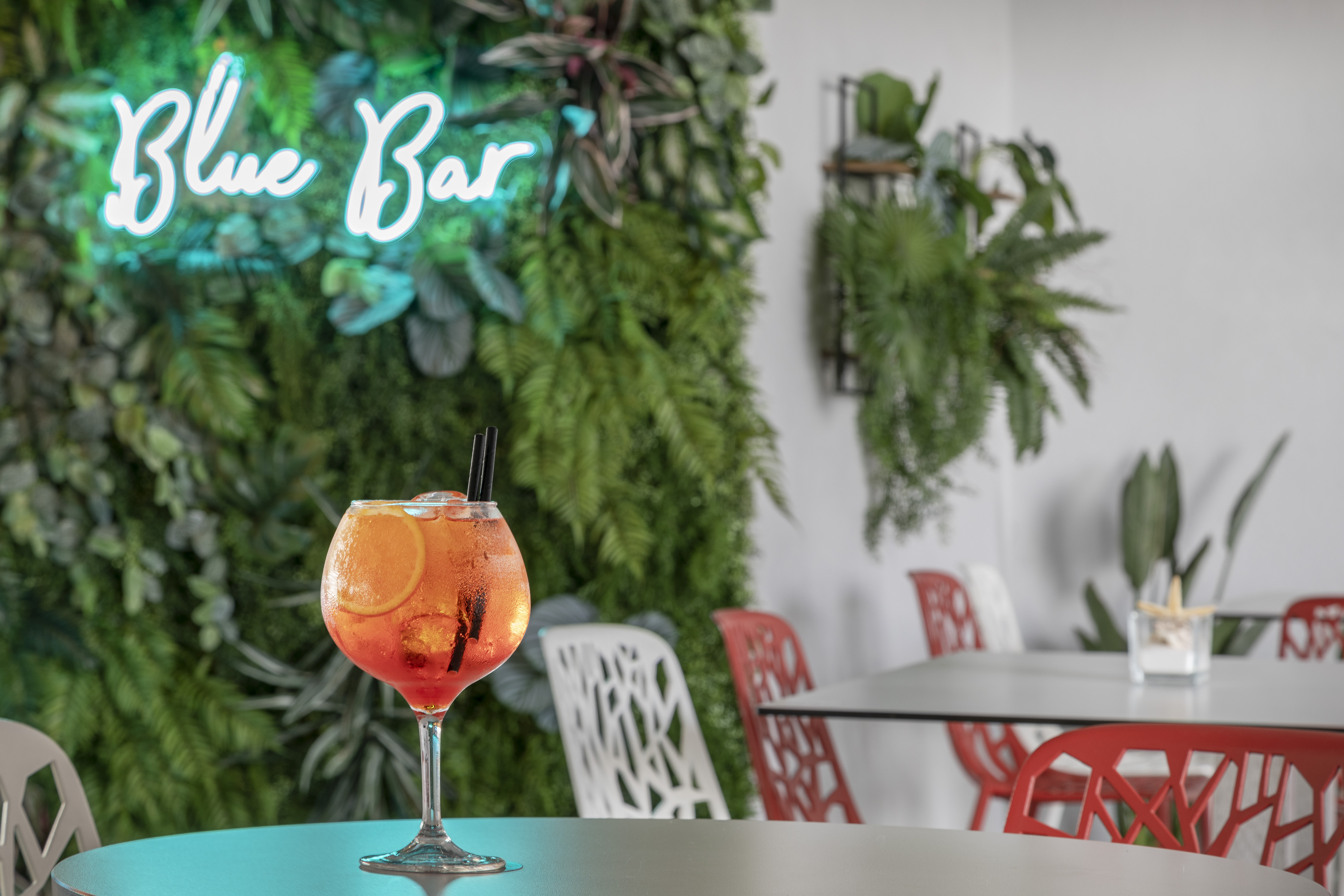 Aperol Spritz cocktail on table at Blue Bar with neon sign and plant wall.