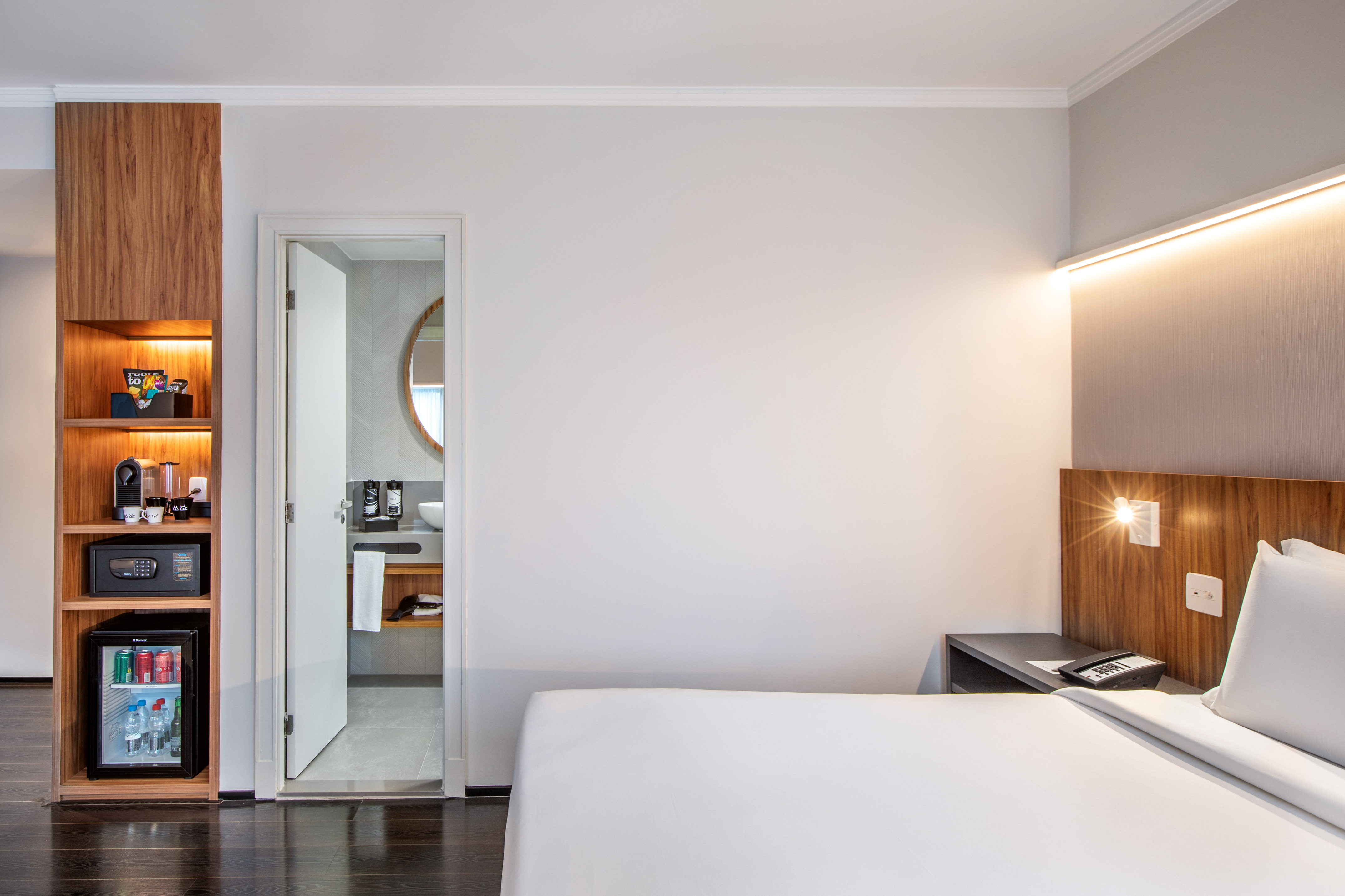 Modern hotel room with bed, minibar, coffee machine, and ensuite bathroom.
