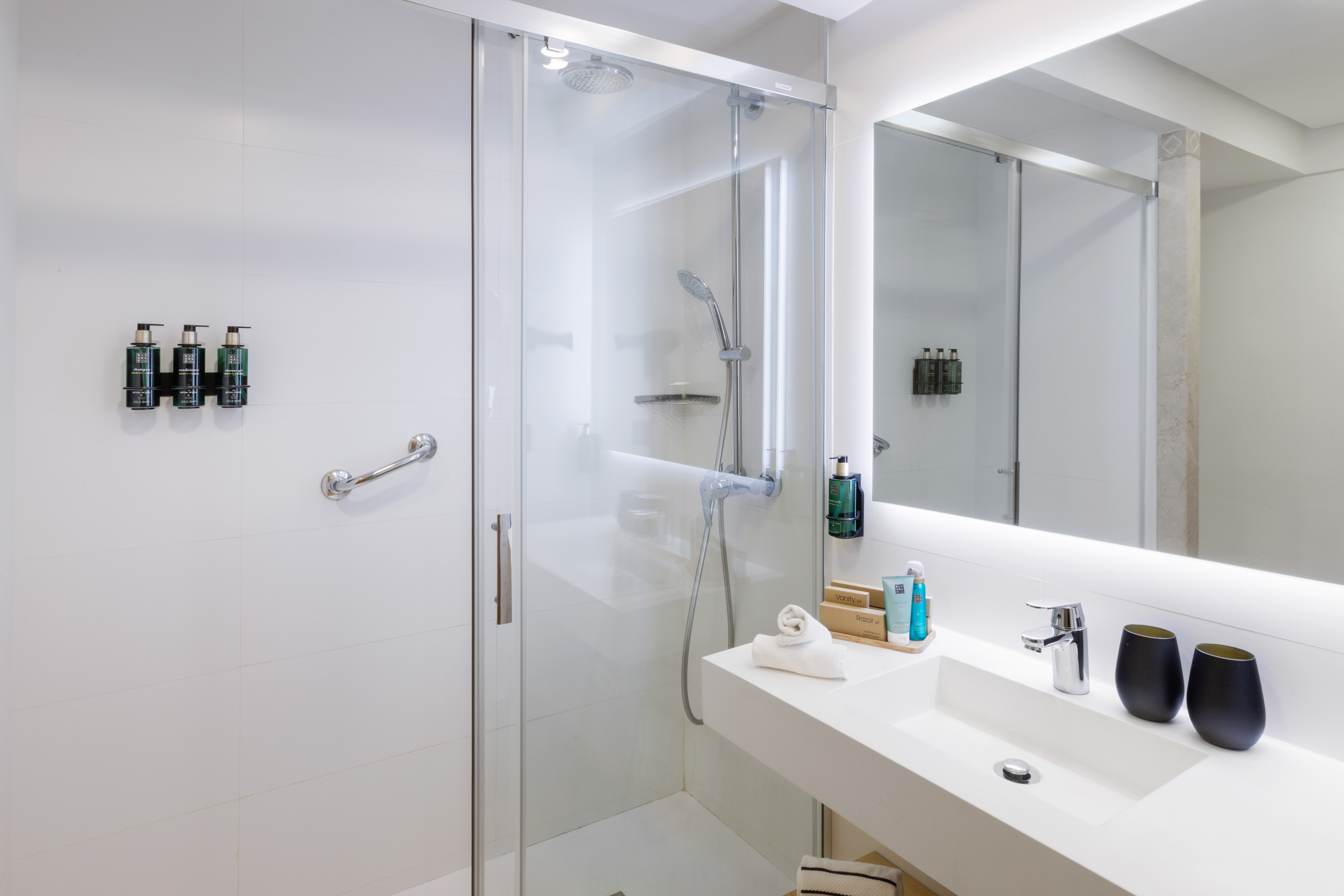 Modern hotel bathroom with glass shower, vanity, and illuminated mirror.