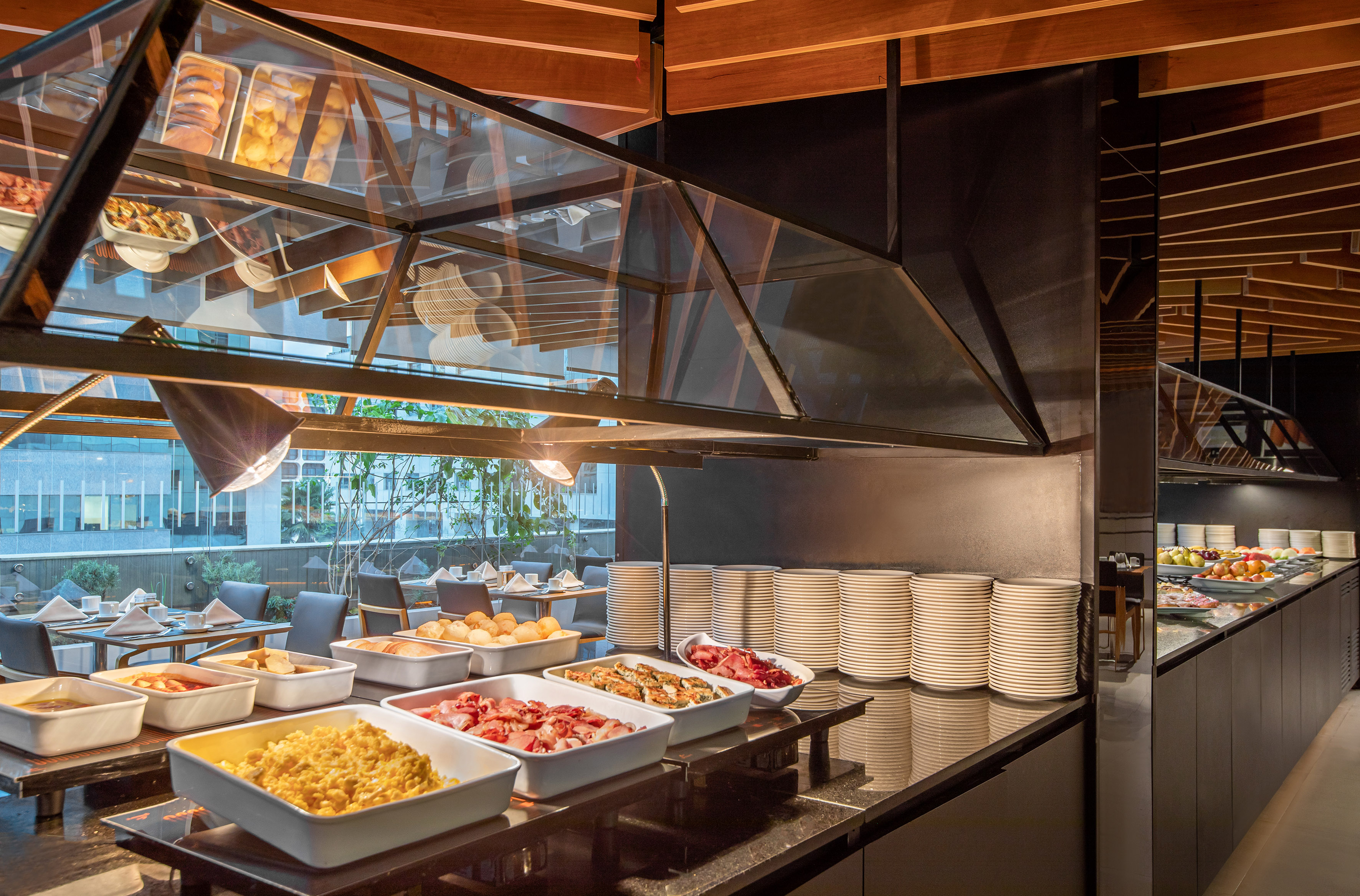 Hotel breakfast buffet with hot food, scrambled eggs, plates, and city view.