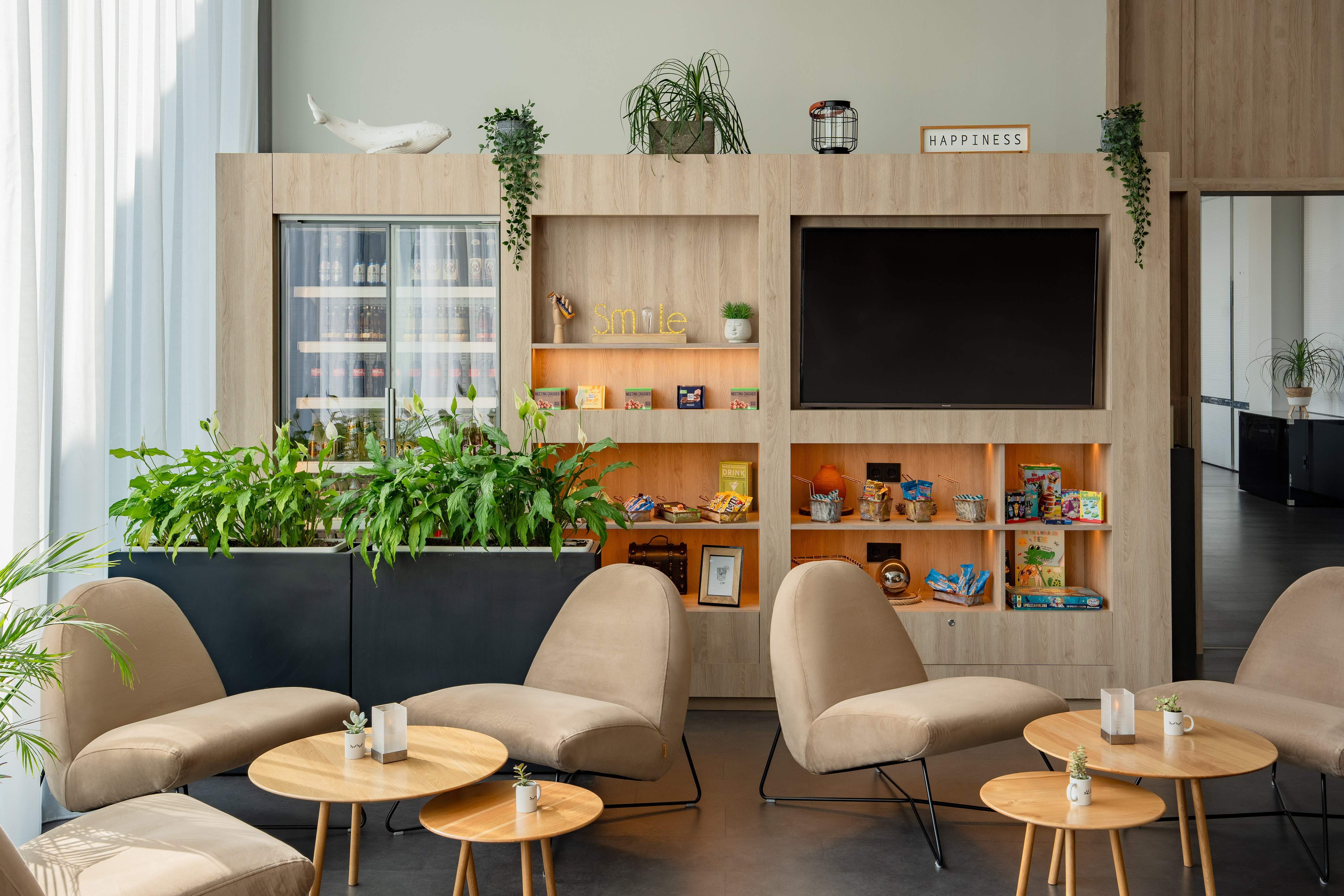 Modern hotel lounge with refreshment bar, TV, and comfortable beige seating.