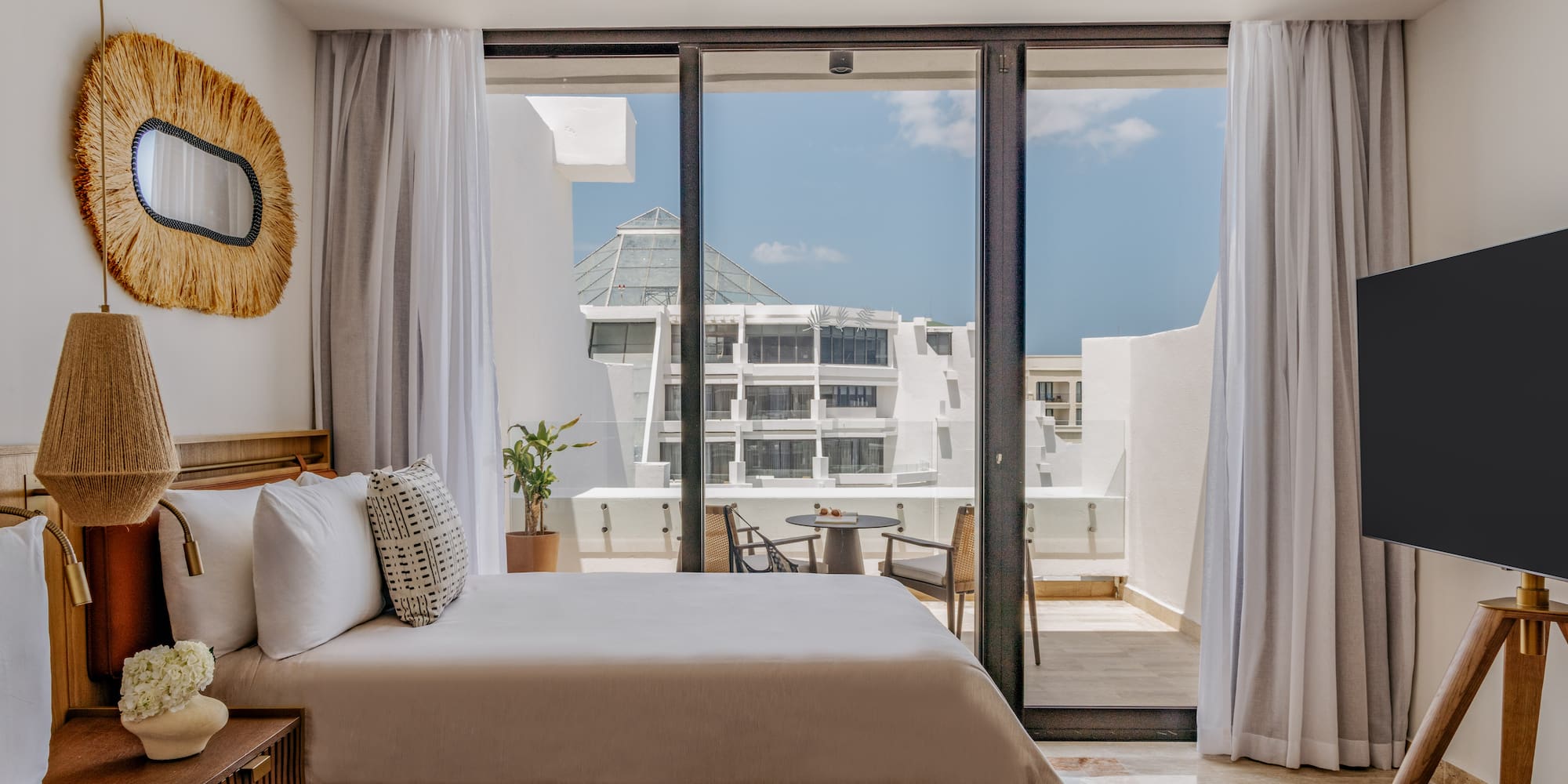 Modern hotel bedroom with balcony, outdoor seating, and resort view.