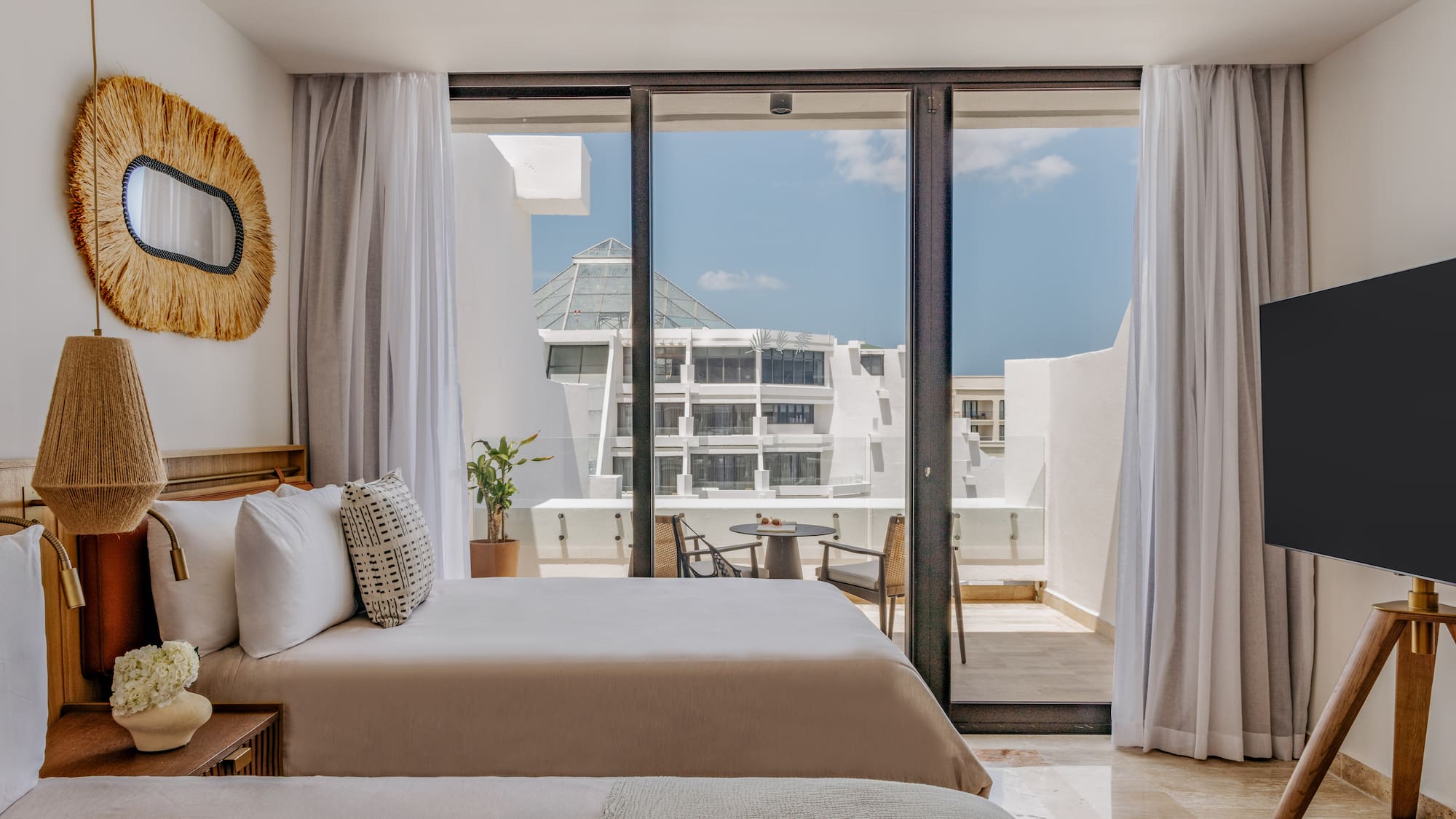 Modern hotel bedroom with balcony, outdoor seating, and resort view.
