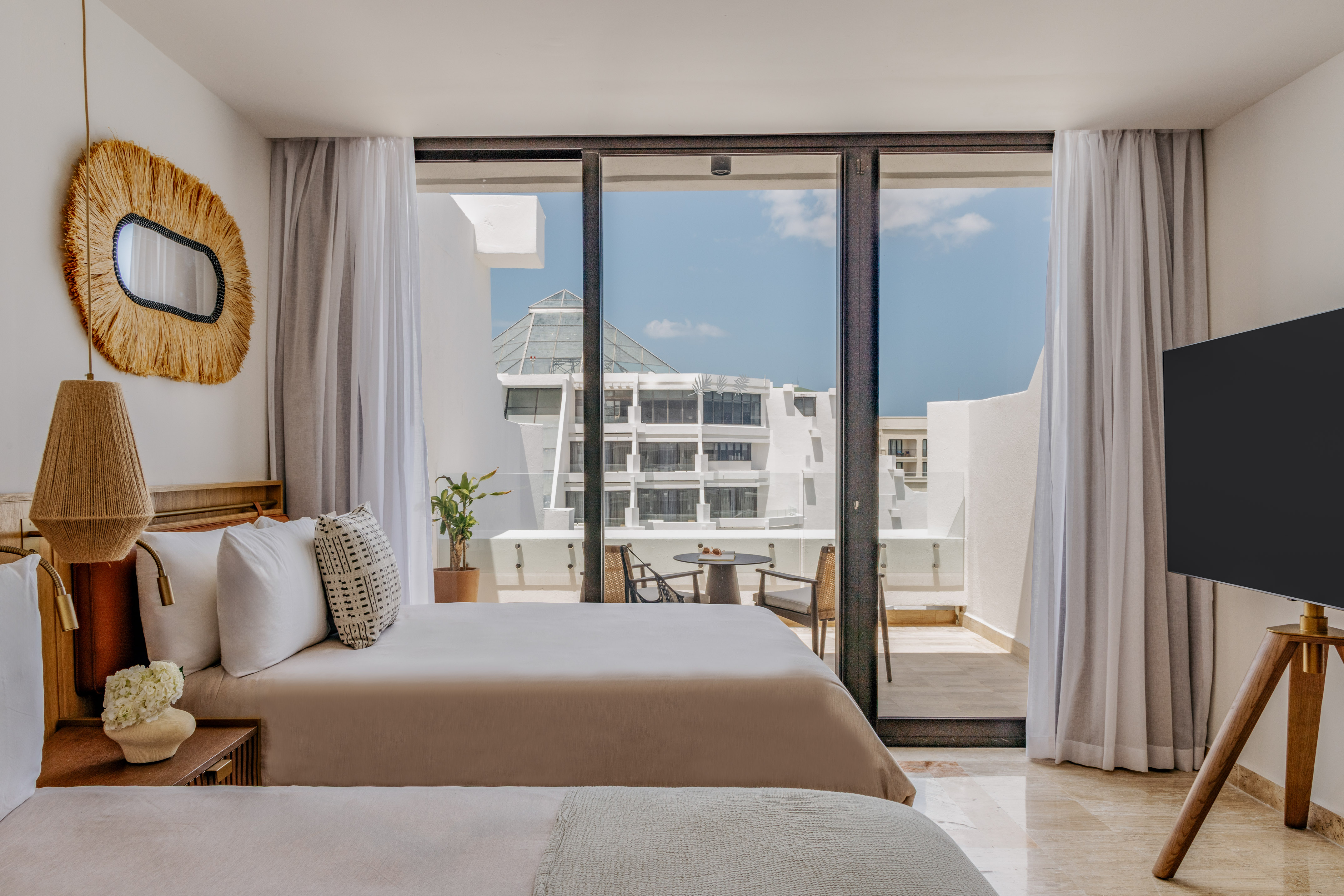 Modern hotel bedroom with balcony, outdoor seating, and resort view.