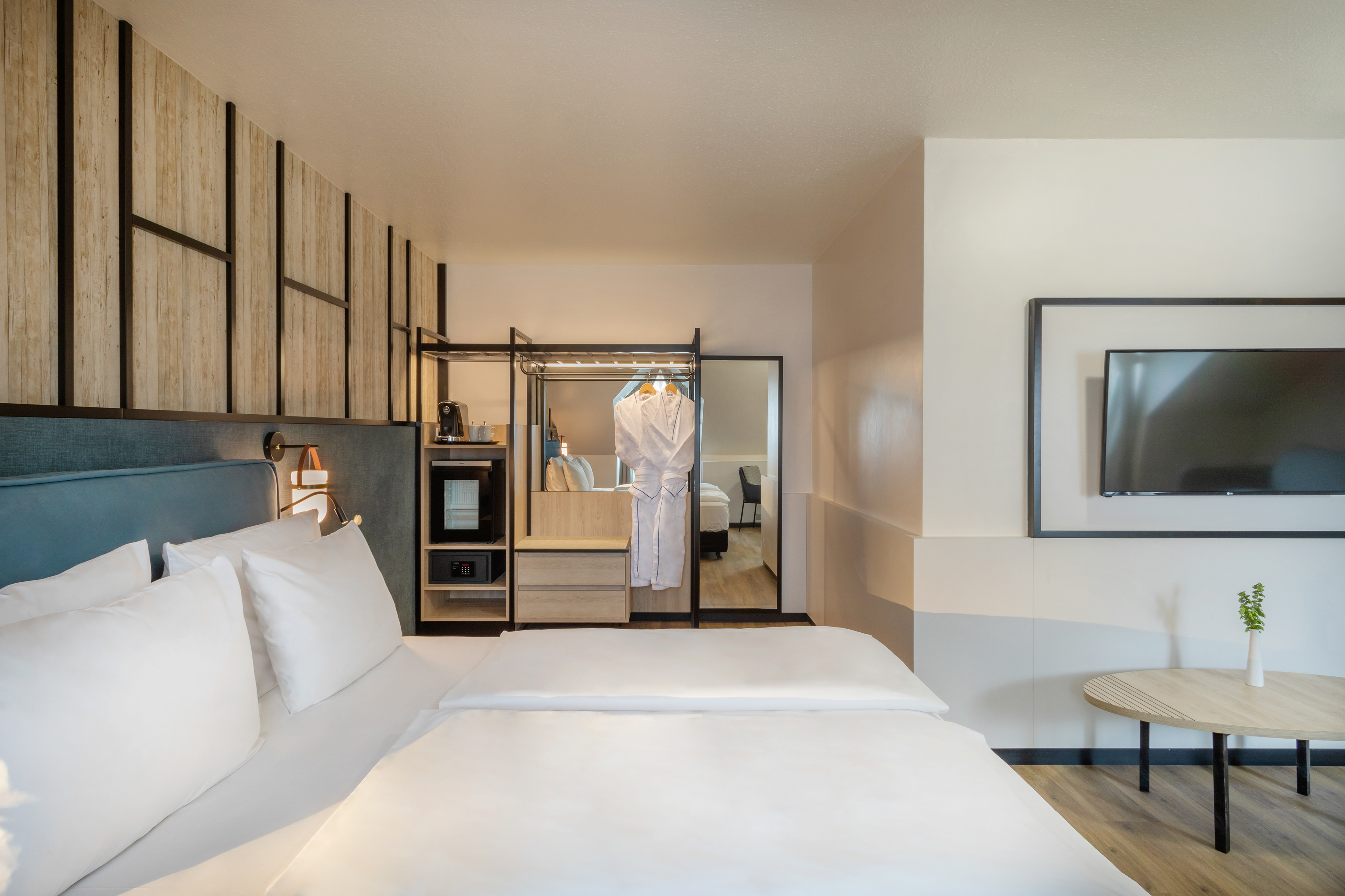Modern hotel bedroom with white bed, TV, open wardrobe, and coffee station.