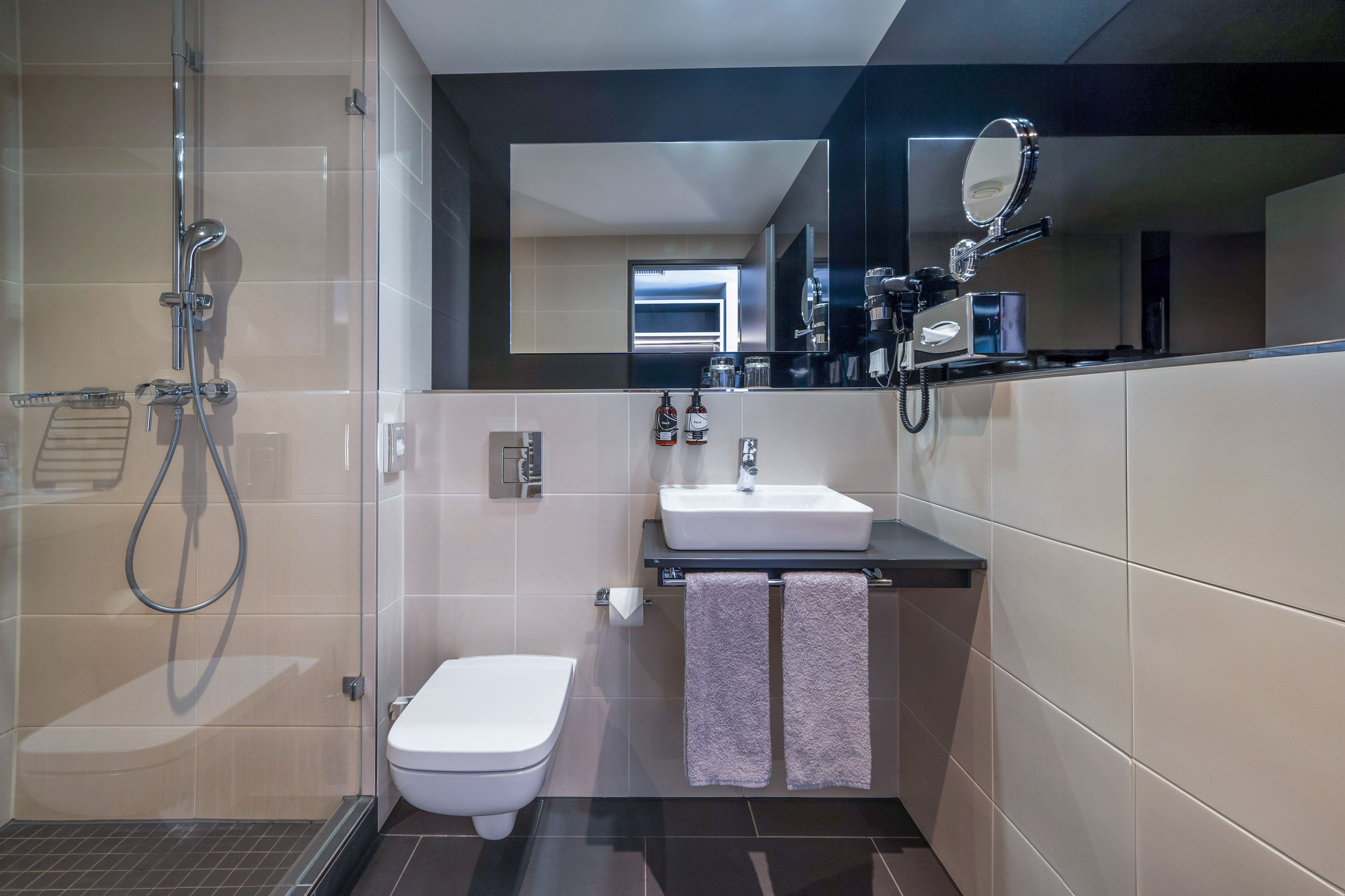 Modern hotel bathroom with glass shower, floating toilet, and vessel sink.