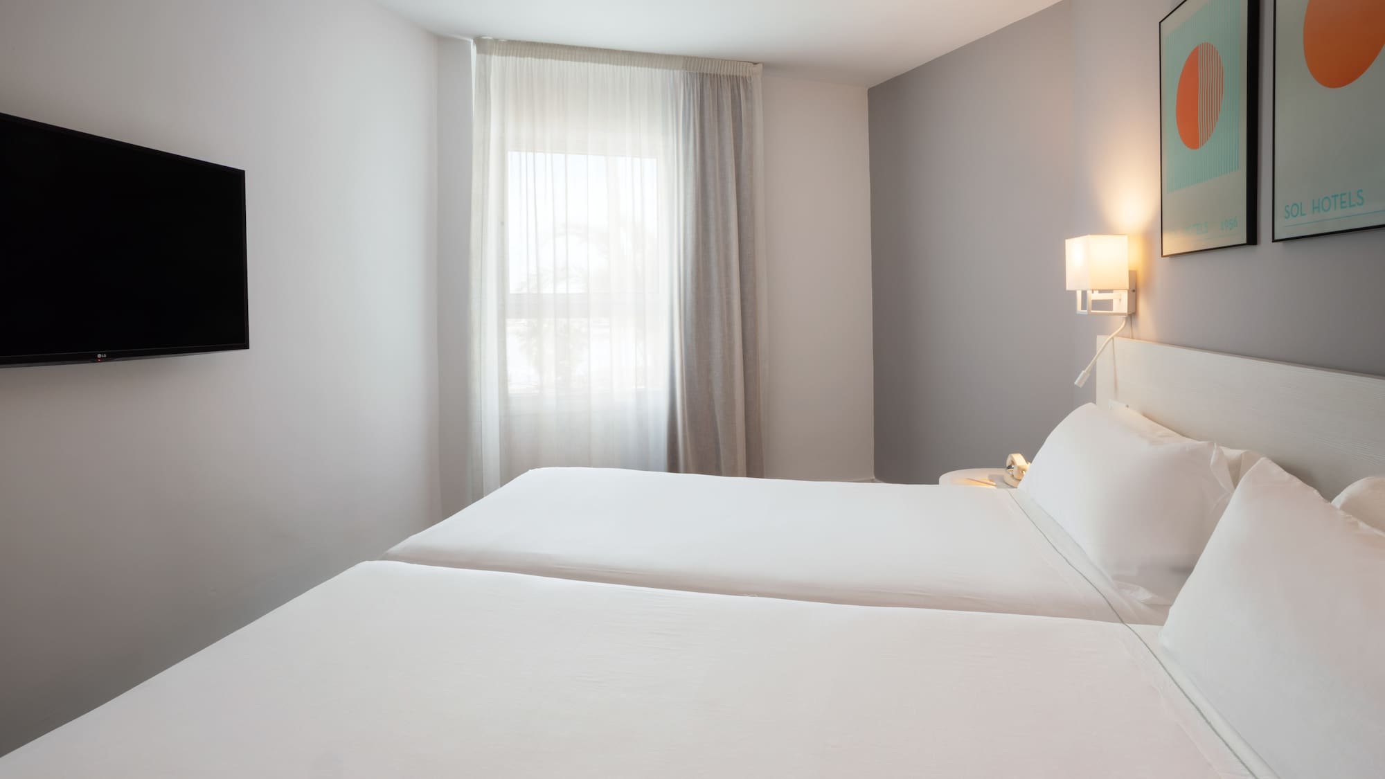 Modern hotel room with twin beds, wall-mounted TV, and window.