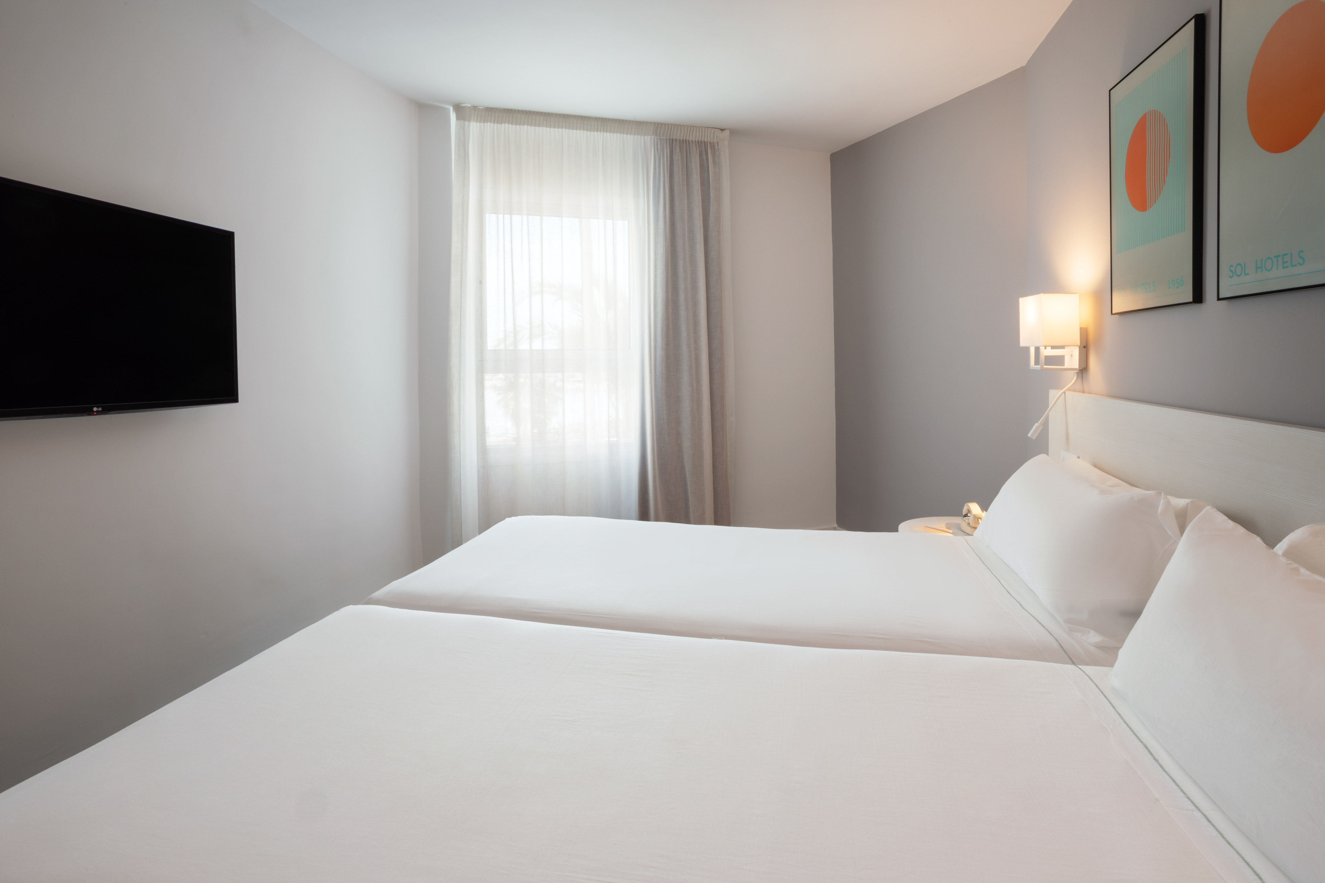 Twin bed hotel room with wall TV, window, and modern decor.