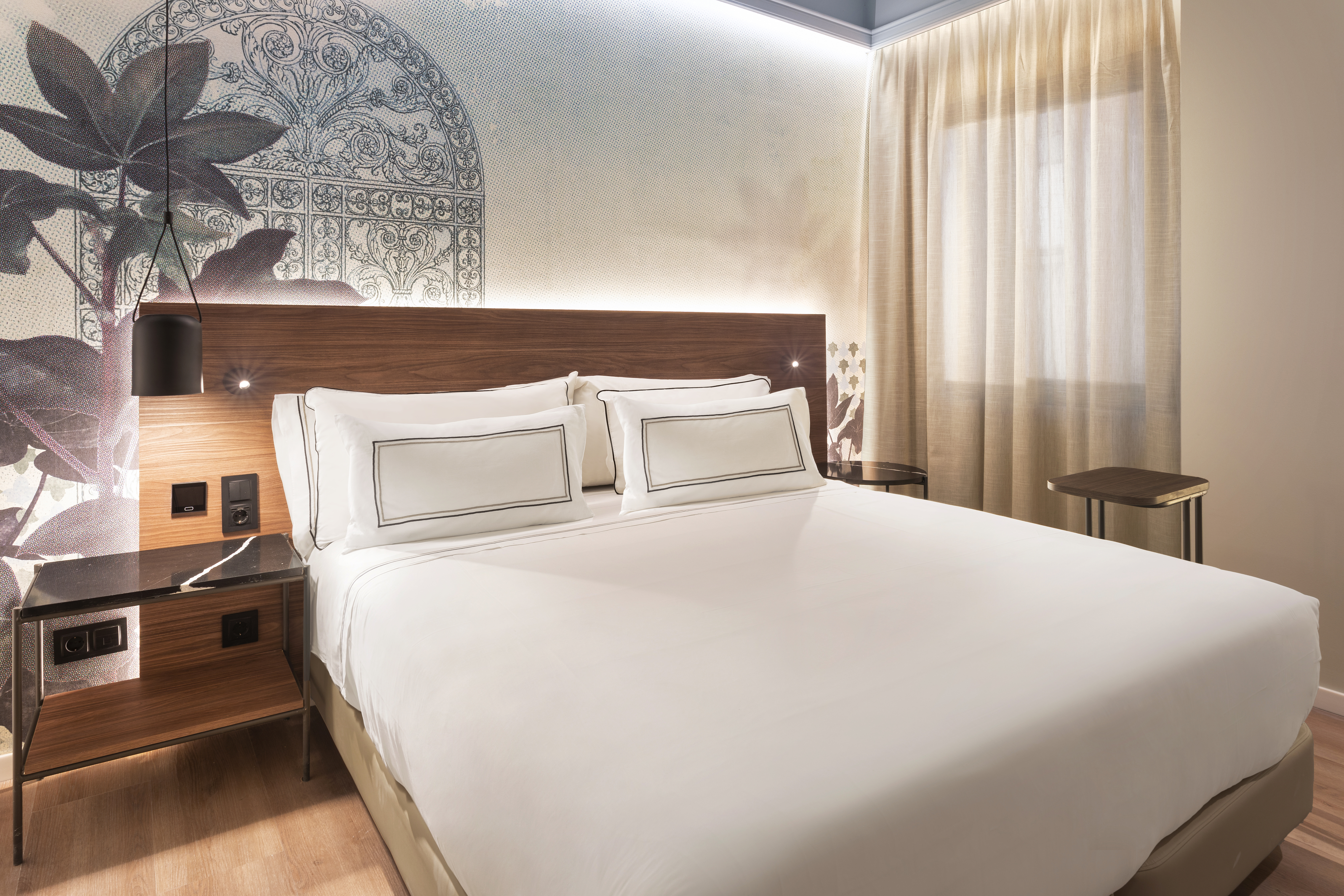 Modern hotel bedroom with white bed, wooden headboard, and patterned wallpaper.