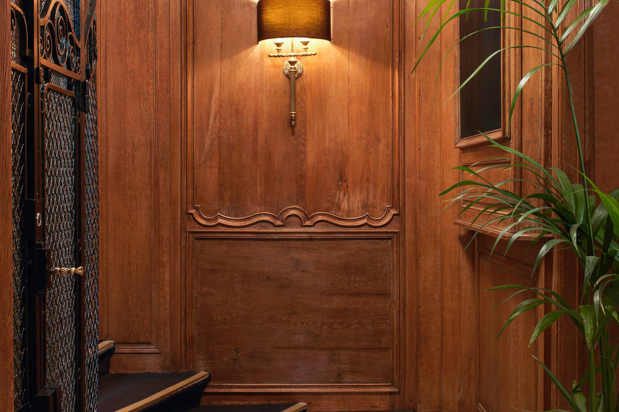 Elegant wood paneling, marble floor, wall sconce, and vintage elevator.