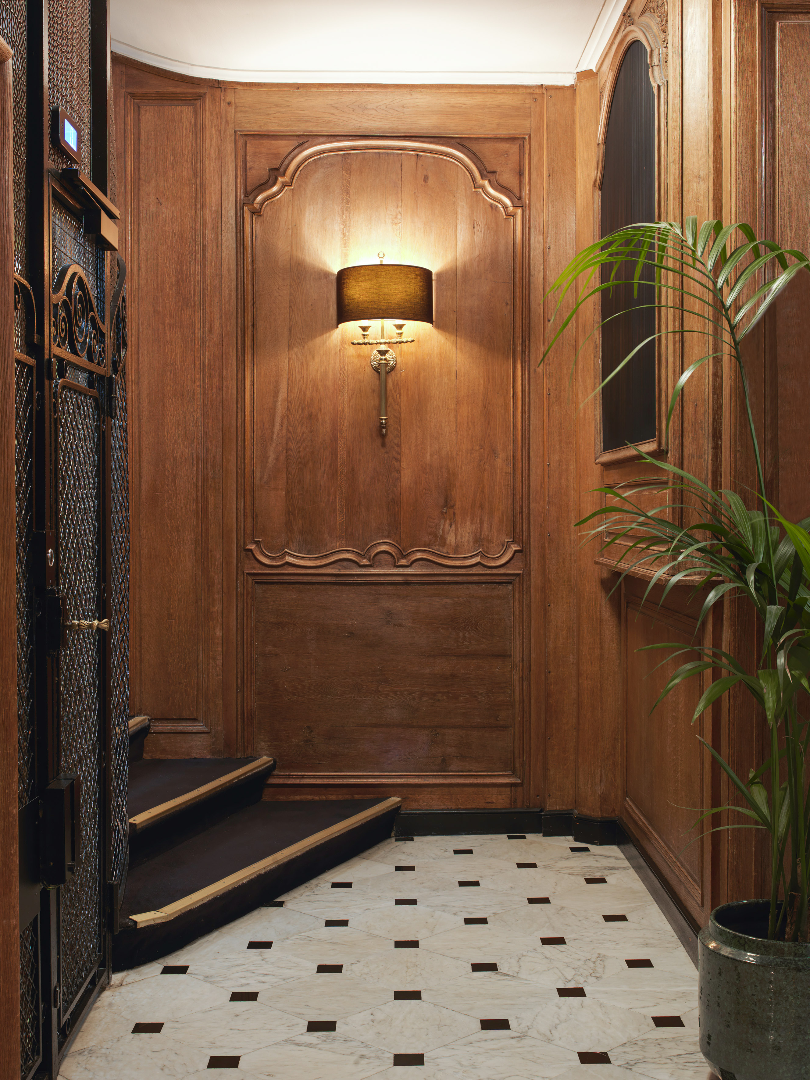 Elegant wood paneling, marble floor, wall sconce, and vintage elevator.