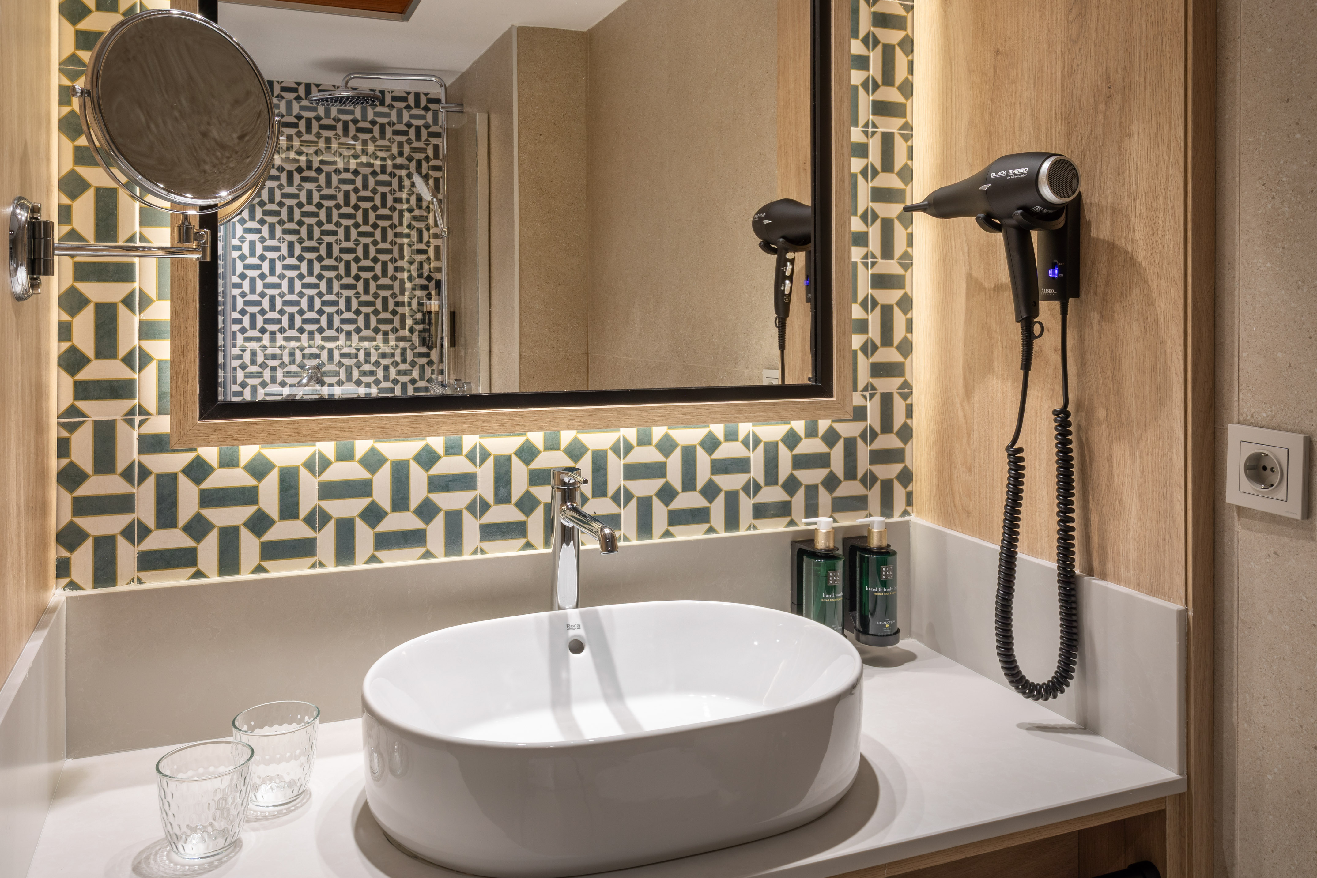 Modern hotel bathroom vanity with sink, mirror, geometric tiles, and hairdryer.