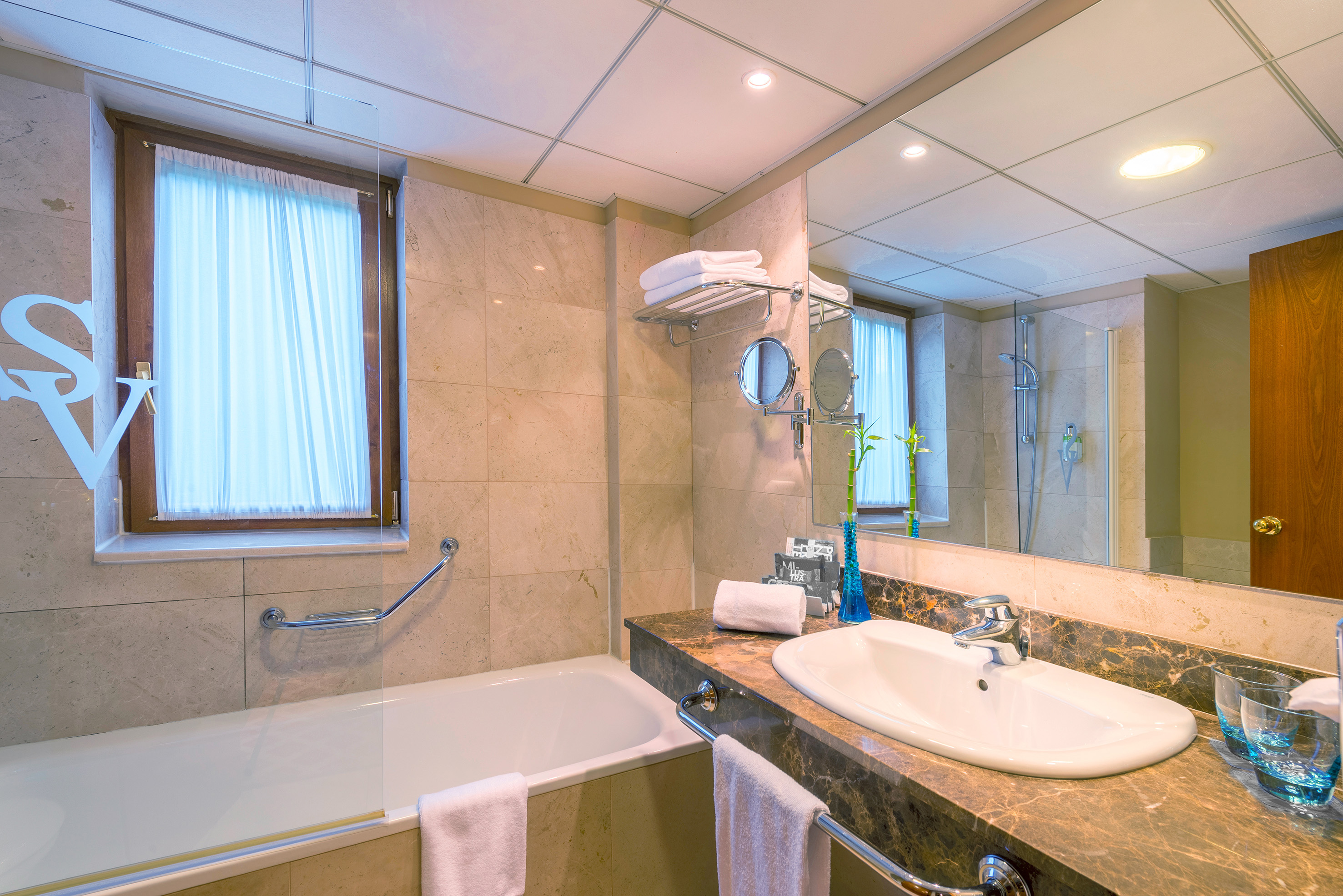Hotel bathroom with bathtub, shower, sink, marble vanity, and mirror.