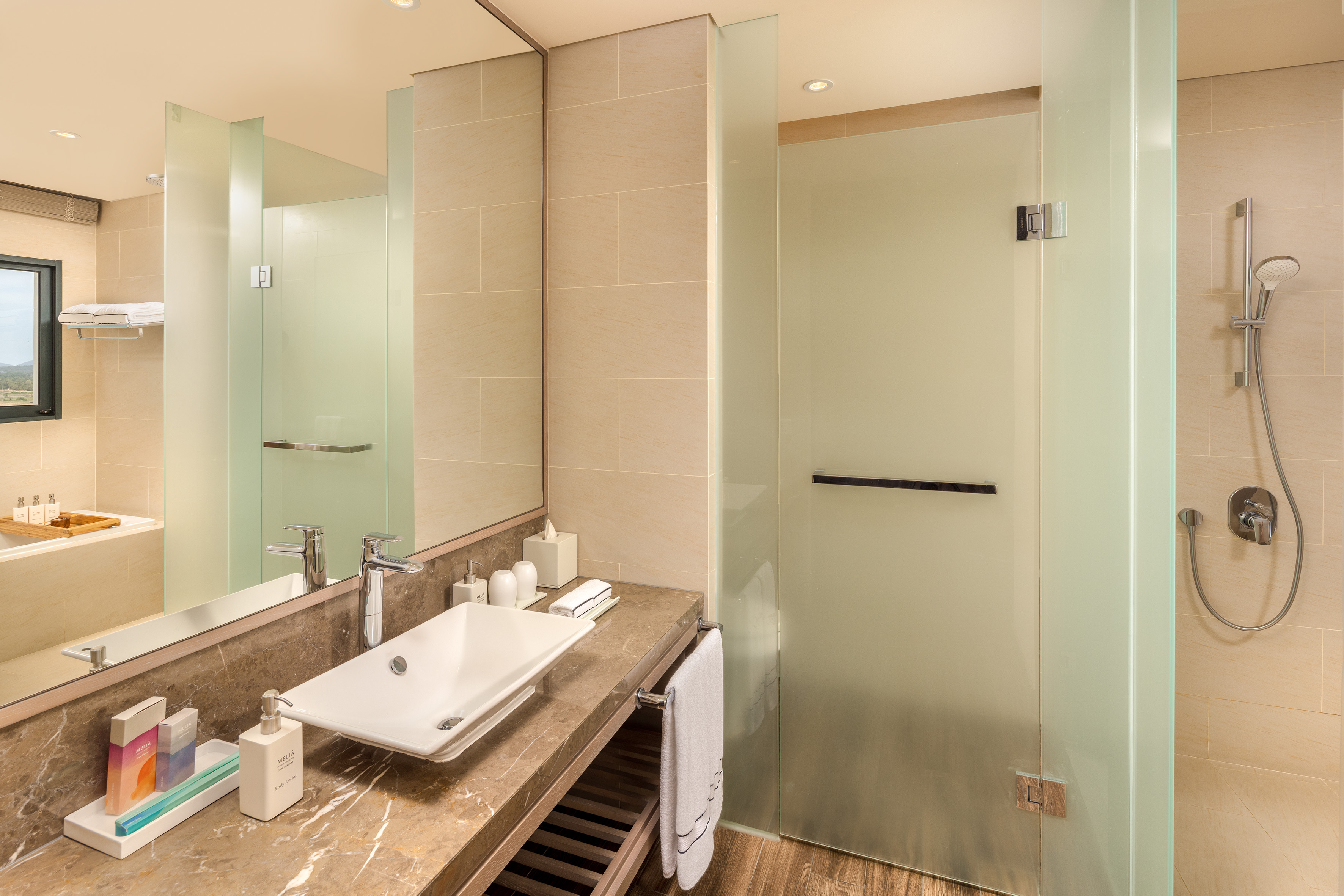 Modern hotel bathroom with marble vanity, sink, and frosted glass shower.