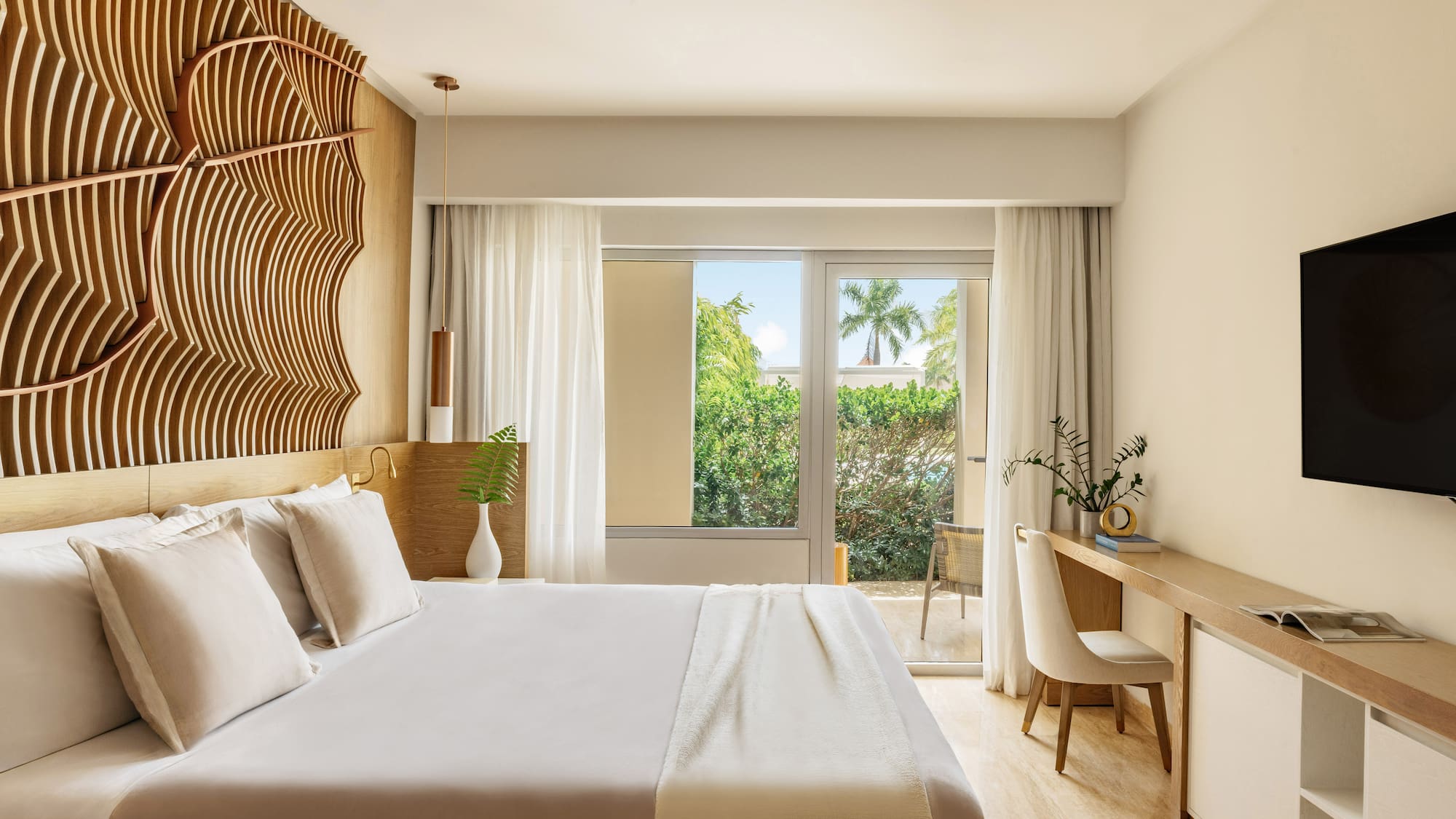 Luxury hotel bedroom with king bed, modern headboard, and tropical view.
