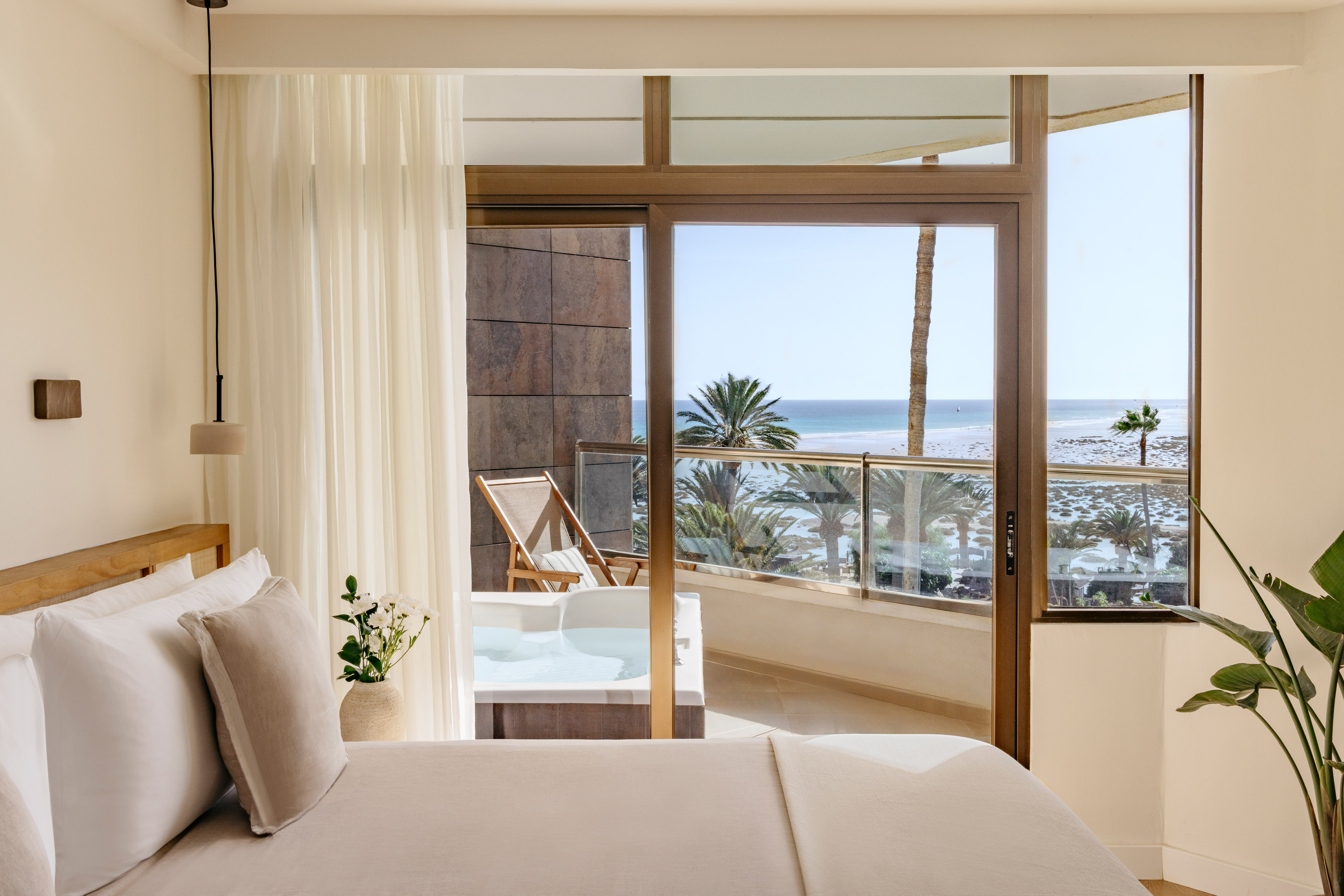 Luxury hotel bedroom with ocean view balcony, hot tub, and palm trees.