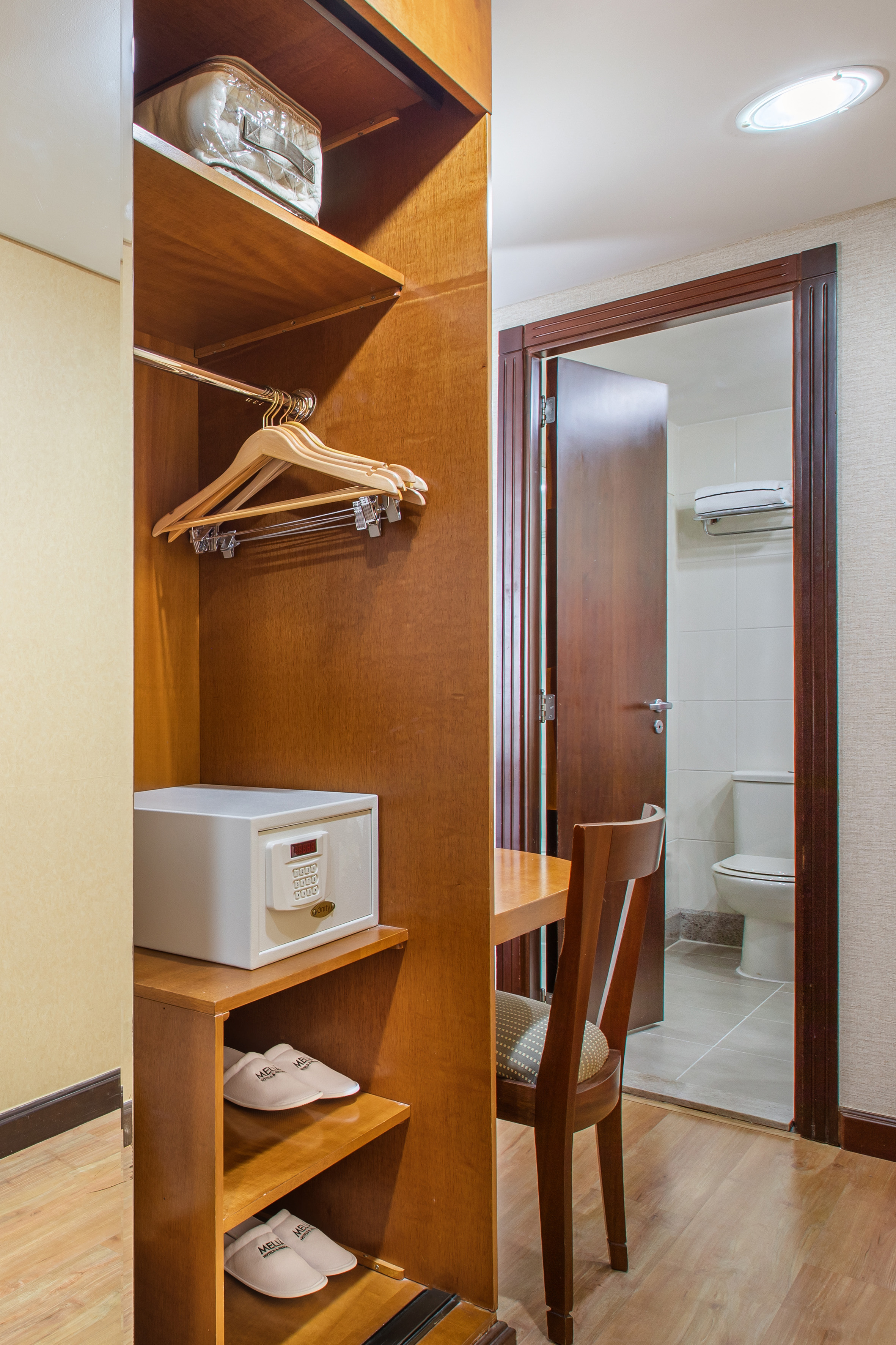 Hotel room closet with safe, hangers, slippers, table, and adjacent bathroom.