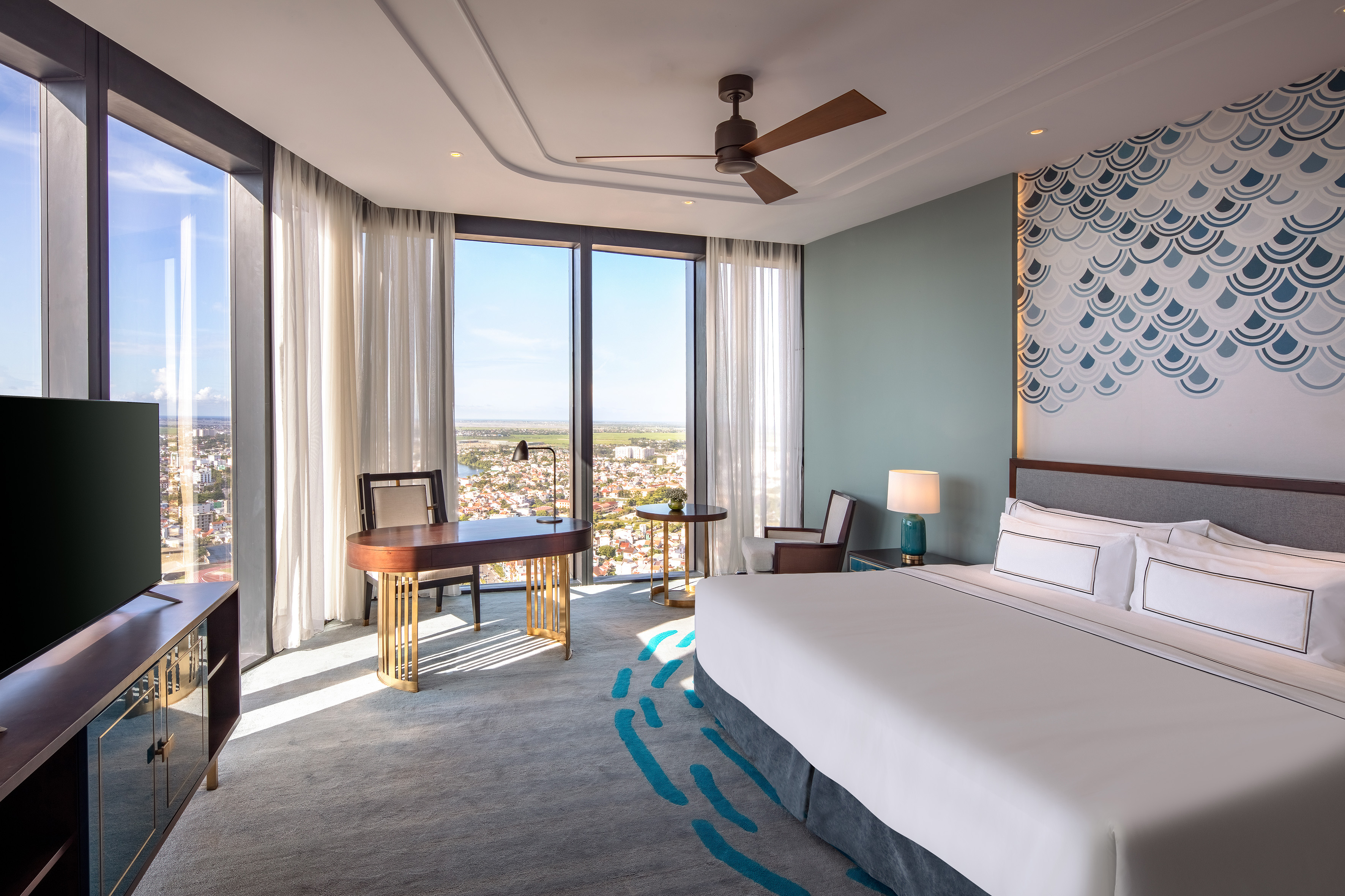Modern hotel suite with city skyline view, king bed, and stylish workspace.