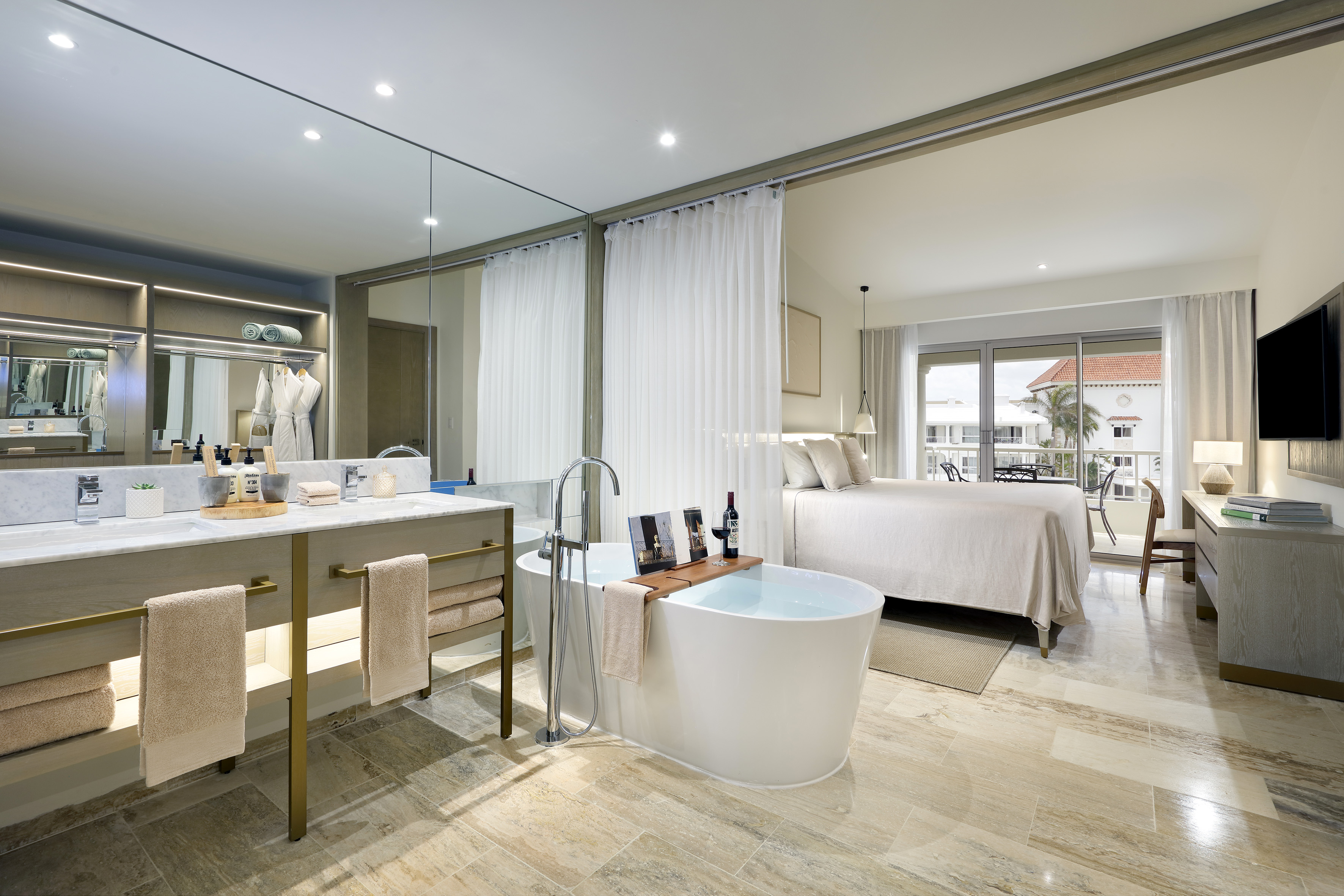 Modern hotel suite with freestanding tub, dual vanity, and king bed.