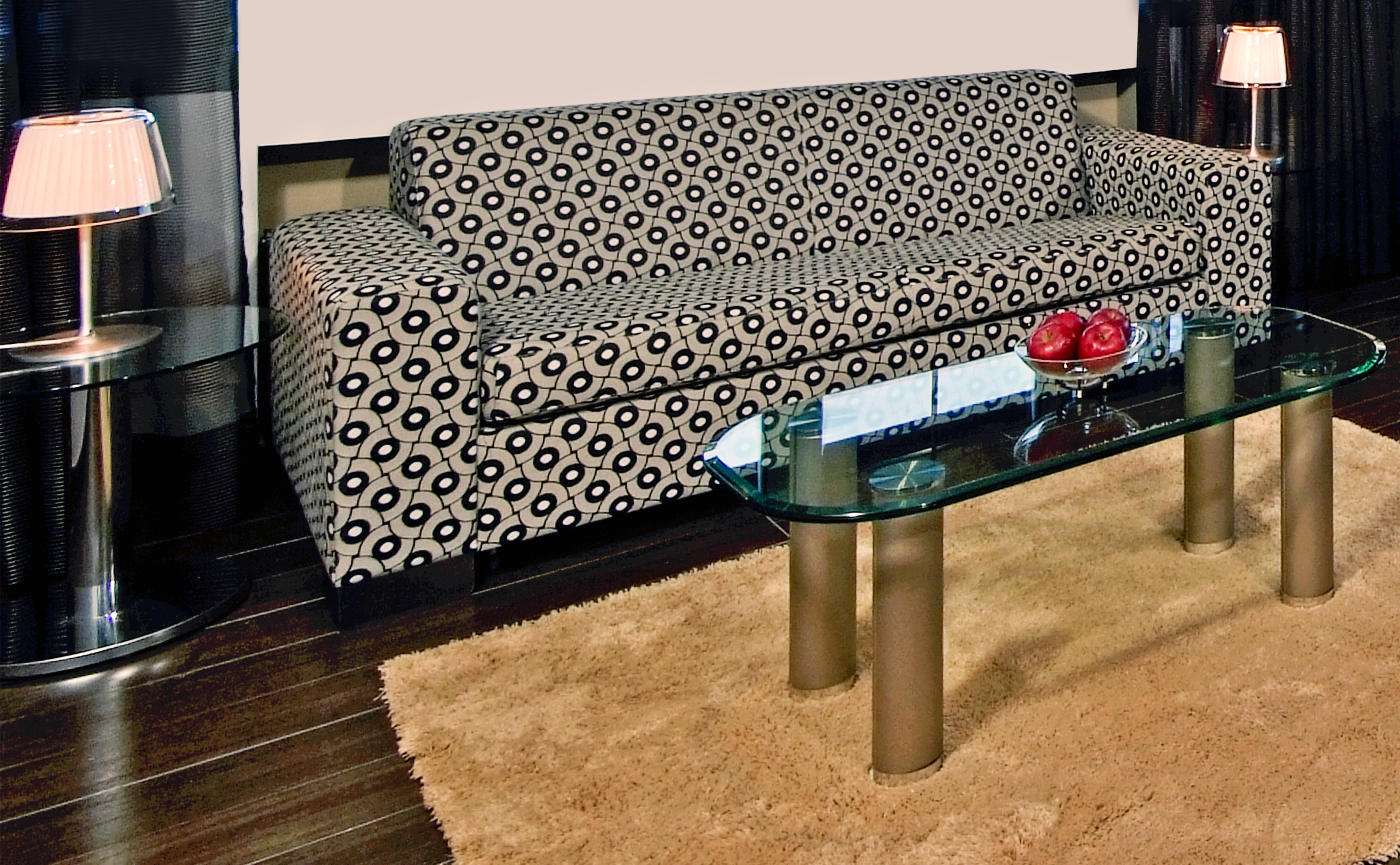 Modern living room with geometric pattern sofa, glass coffee table, and shaggy rug.