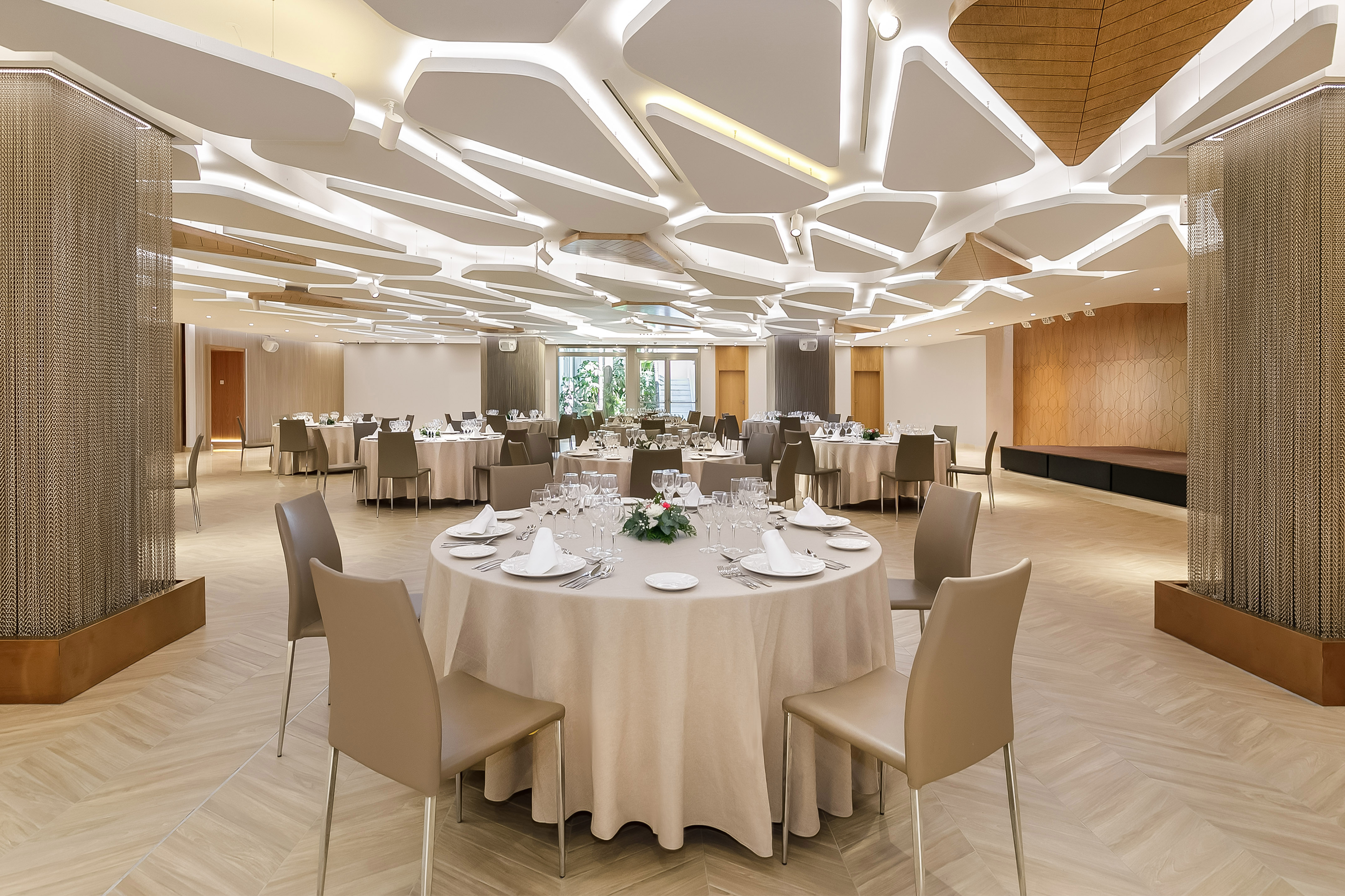Elegant event space with round tables, geometric ceiling design, and modern decor.
