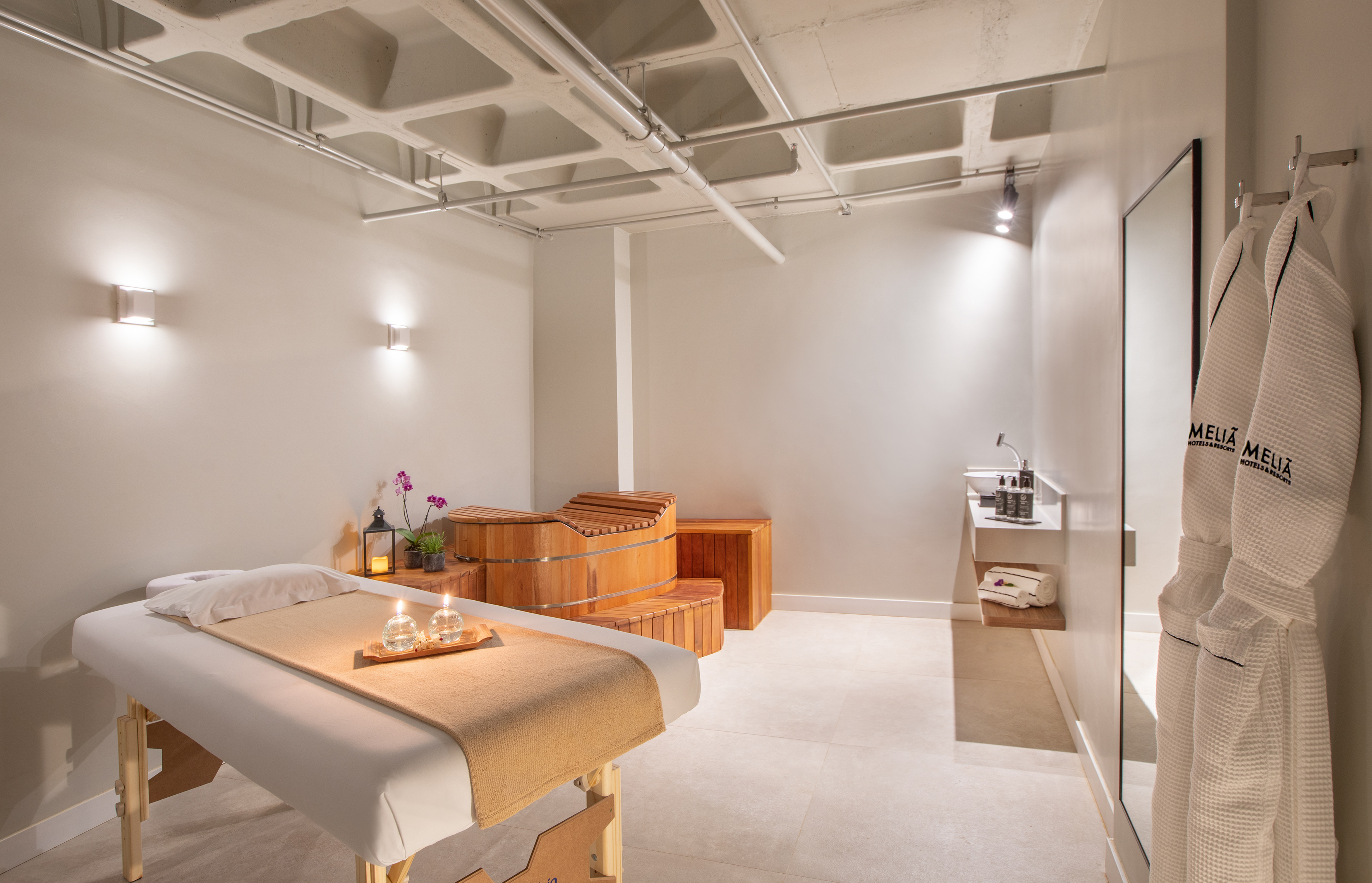 Meliá hotel spa room with massage table, wooden bath, and hanging robes.