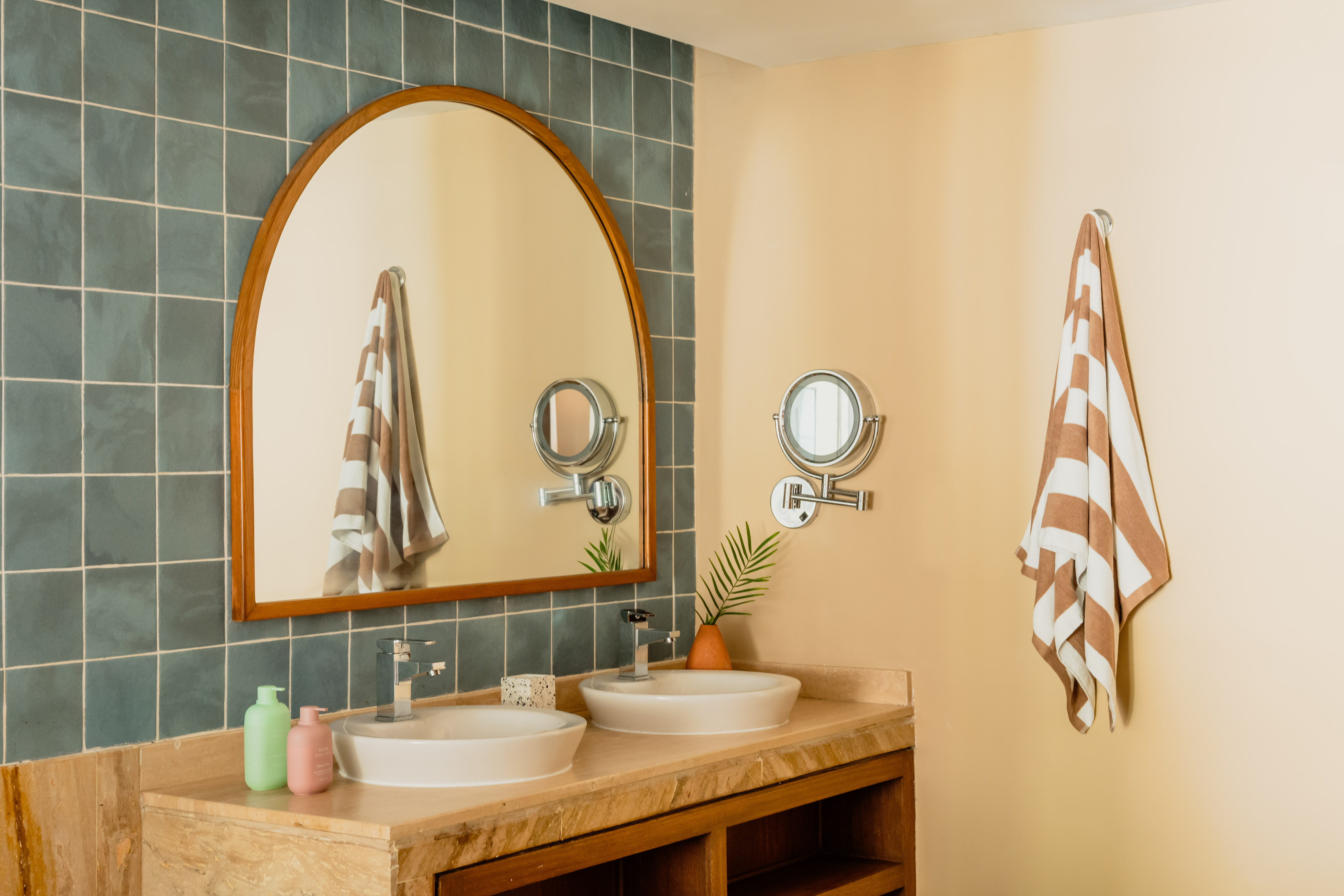 Modern bathroom with double vanity, arched mirror, blue tiles, striped towel.