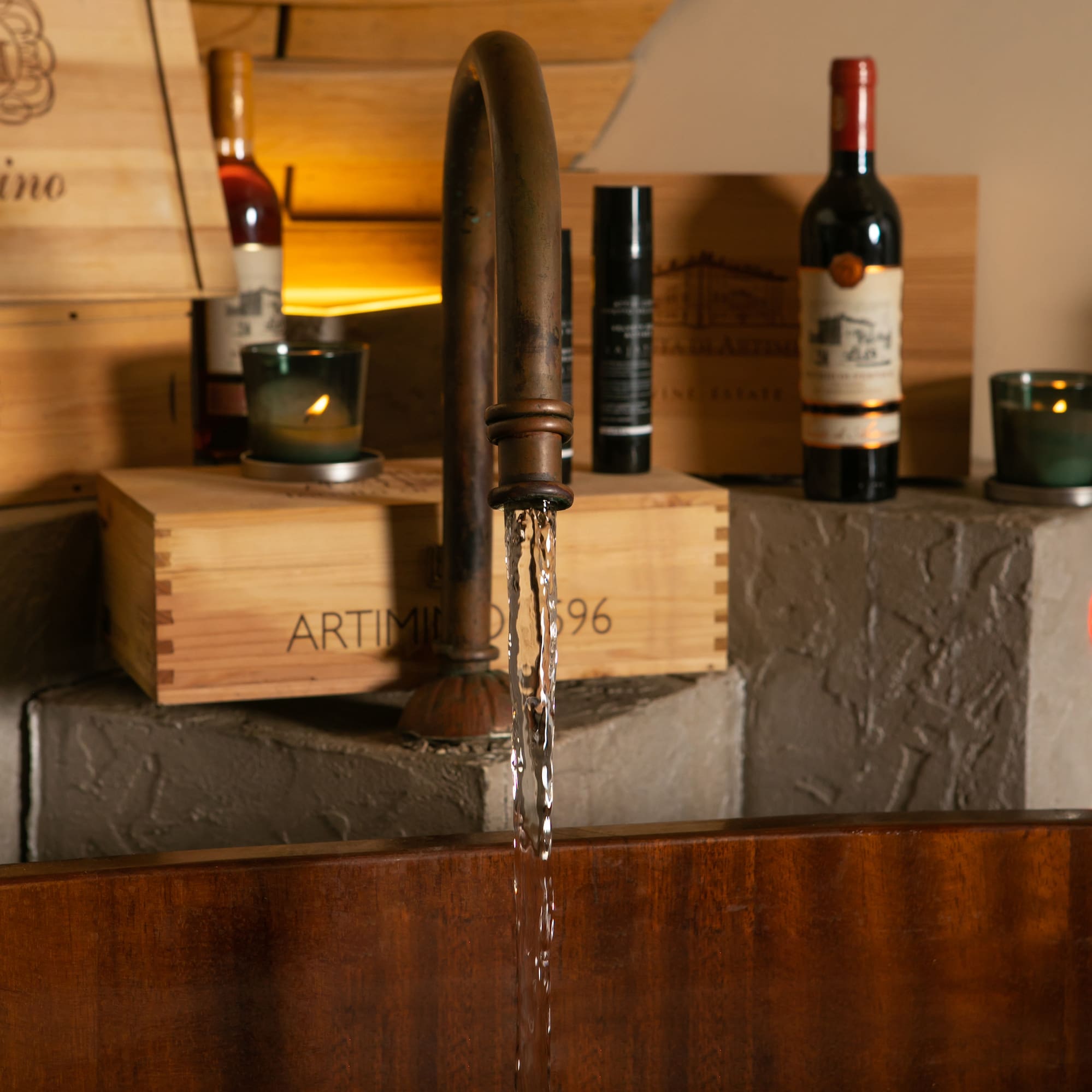 Rustic bronze faucet pouring water into wooden basin, surrounded by wine crates.