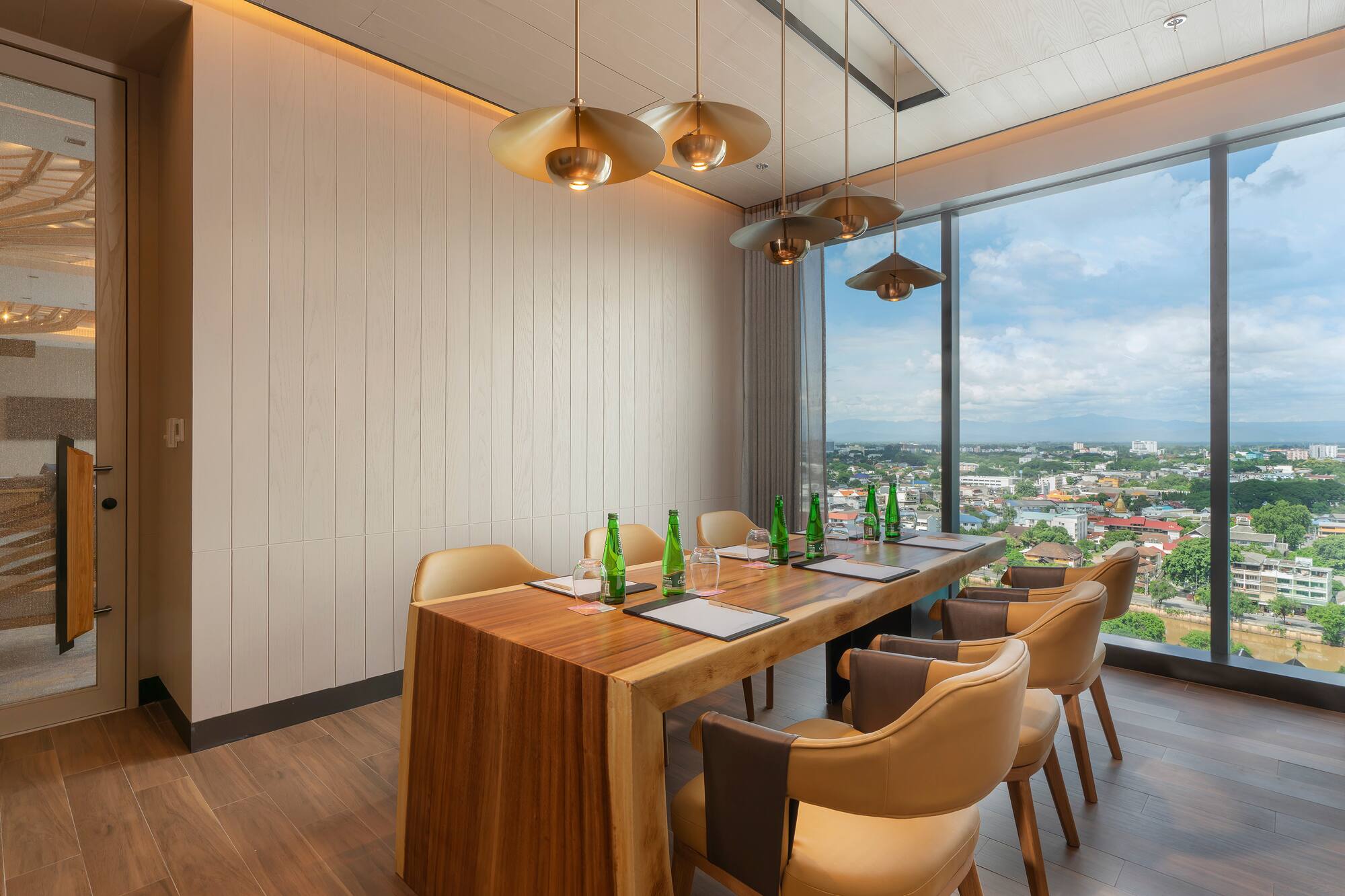 Modern meeting room with large wooden table, gold pendant lights, and panoramic city view.