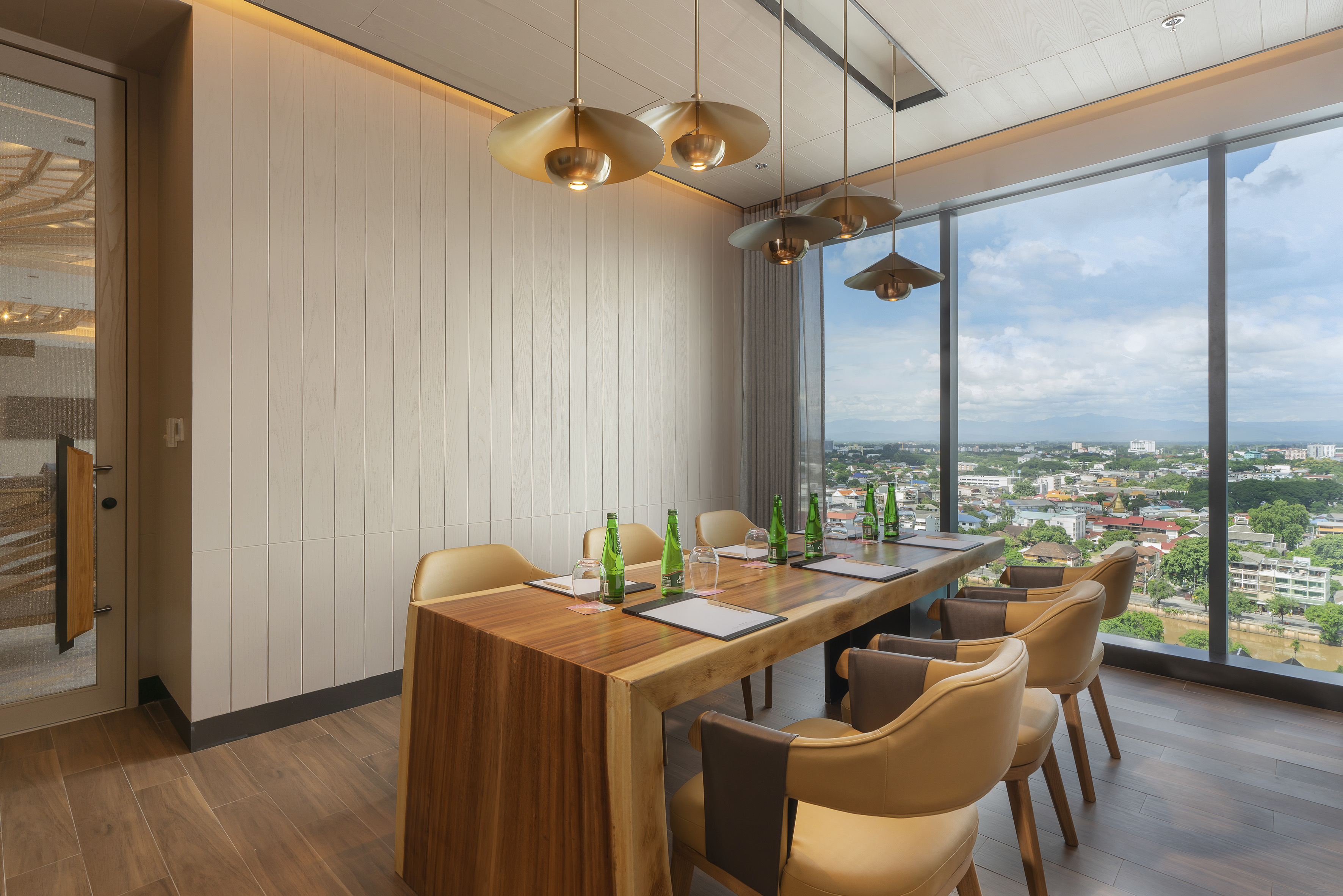 Modern meeting room with large wooden table, gold pendant lights, and panoramic city view.