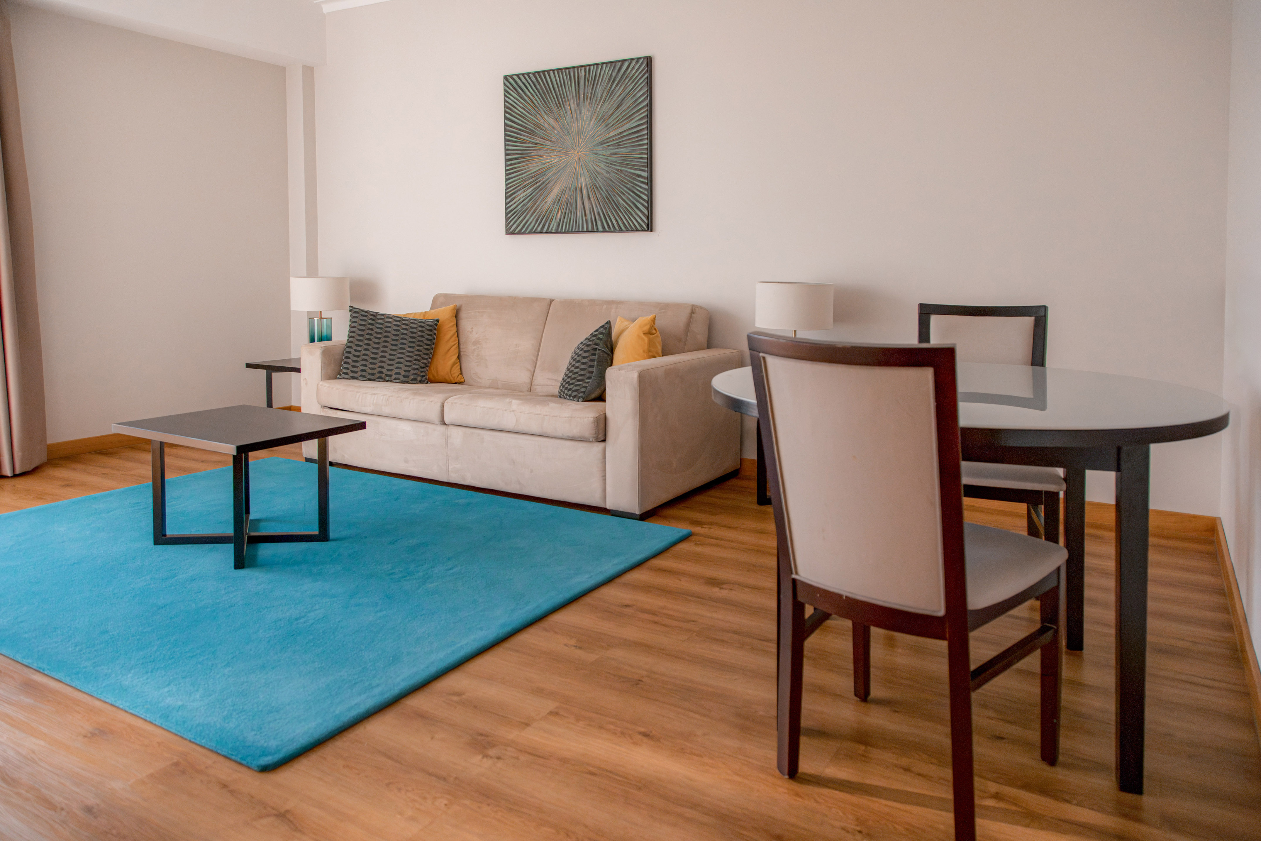 Modern living room with beige sofa, blue rug, coffee table, and dining area.