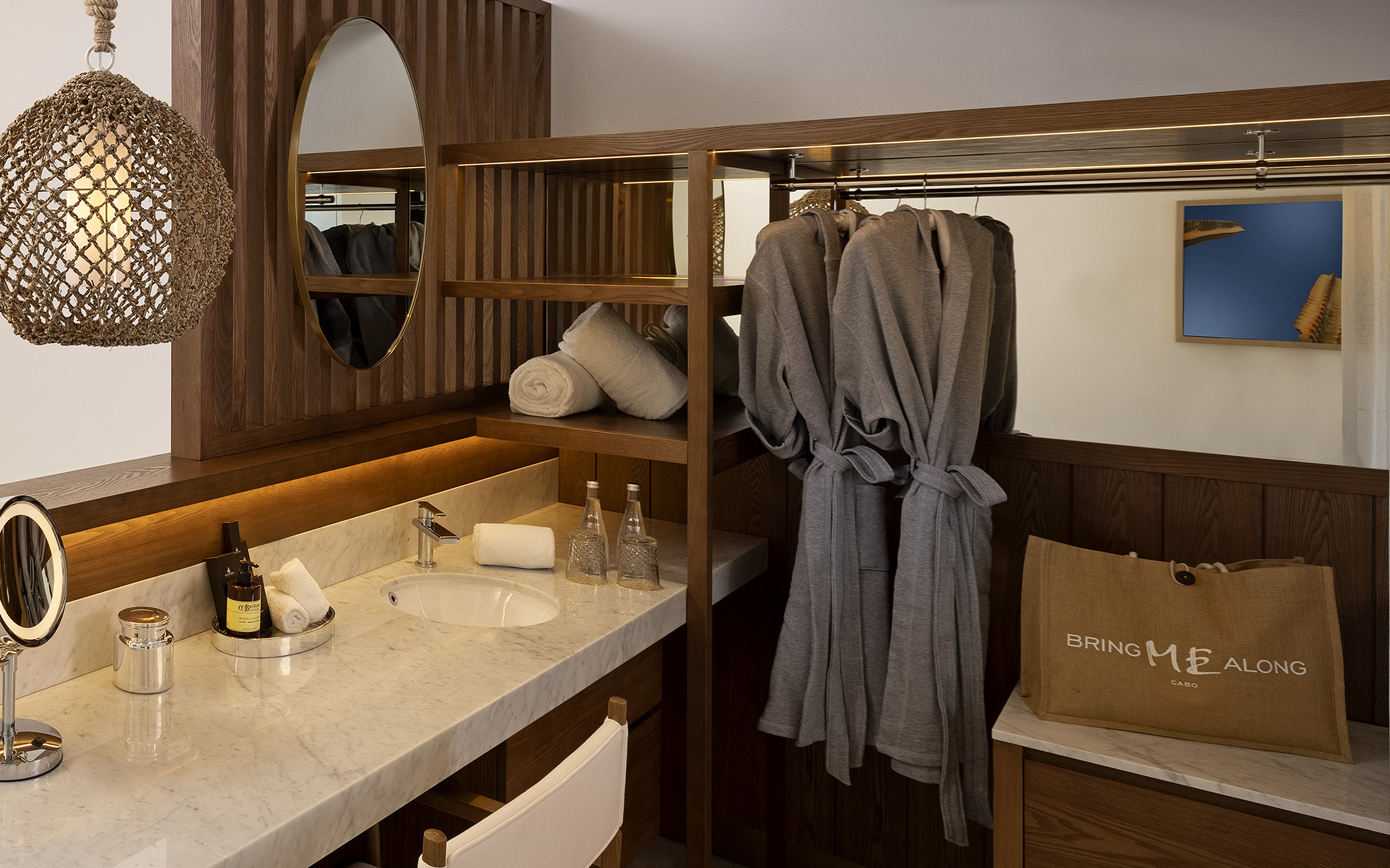 Hotel bathroom vanity, marble counter, wooden shelves, bathrobes.