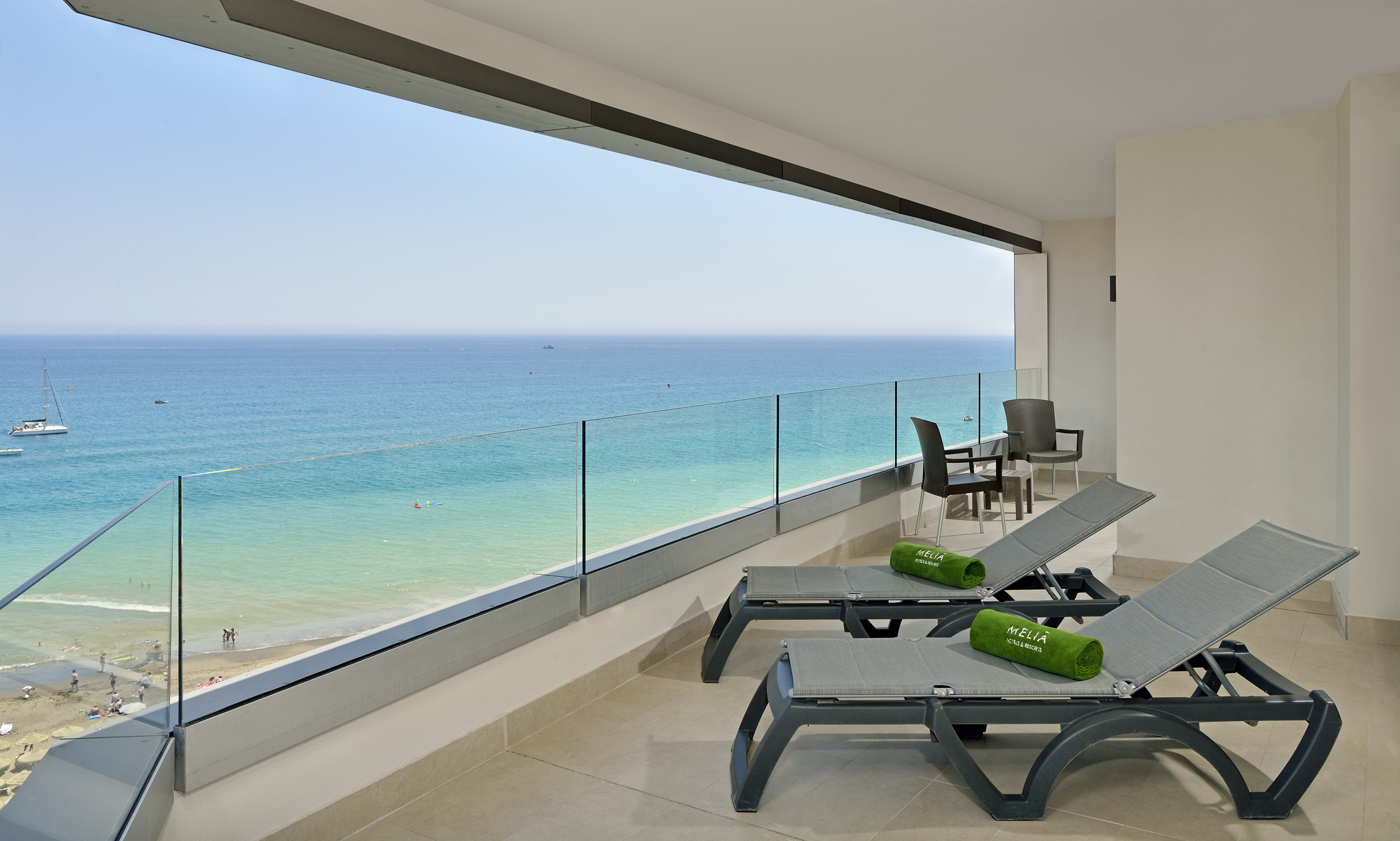 Hotel balcony with panoramic ocean view, beach, and sun loungers.