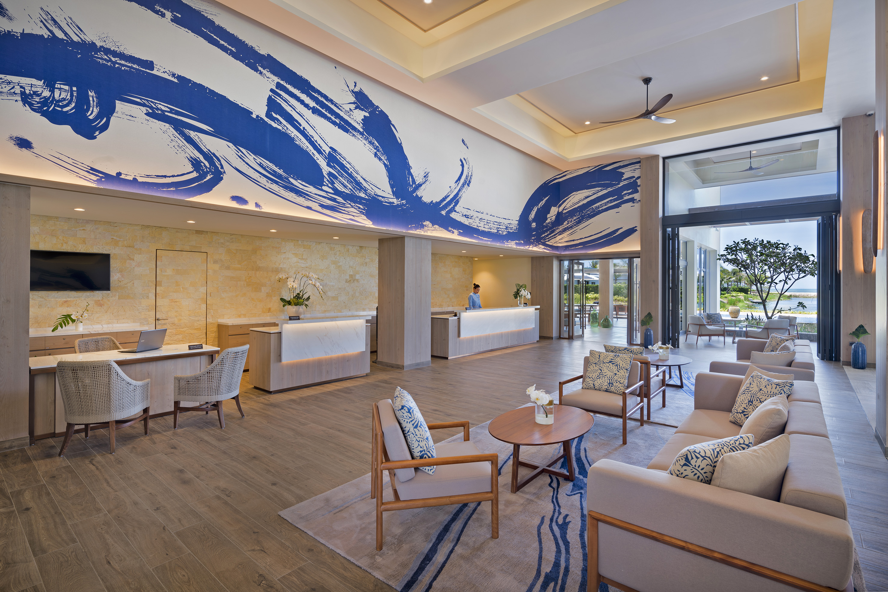 Luxury hotel lobby with blue abstract mural, reception, and beach view.