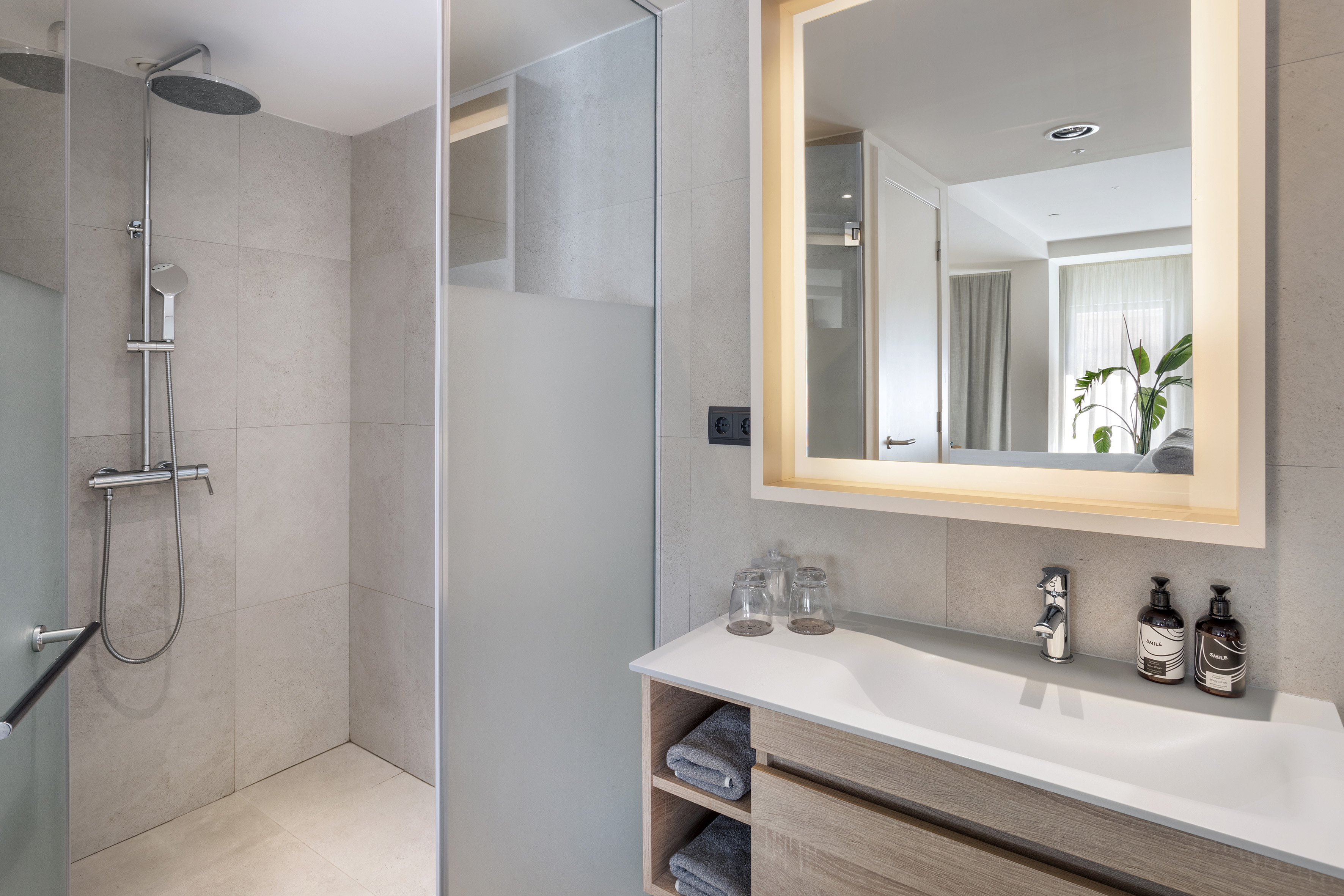 Modern bathroom with walk-in shower, sleek wooden vanity, and illuminated mirror.