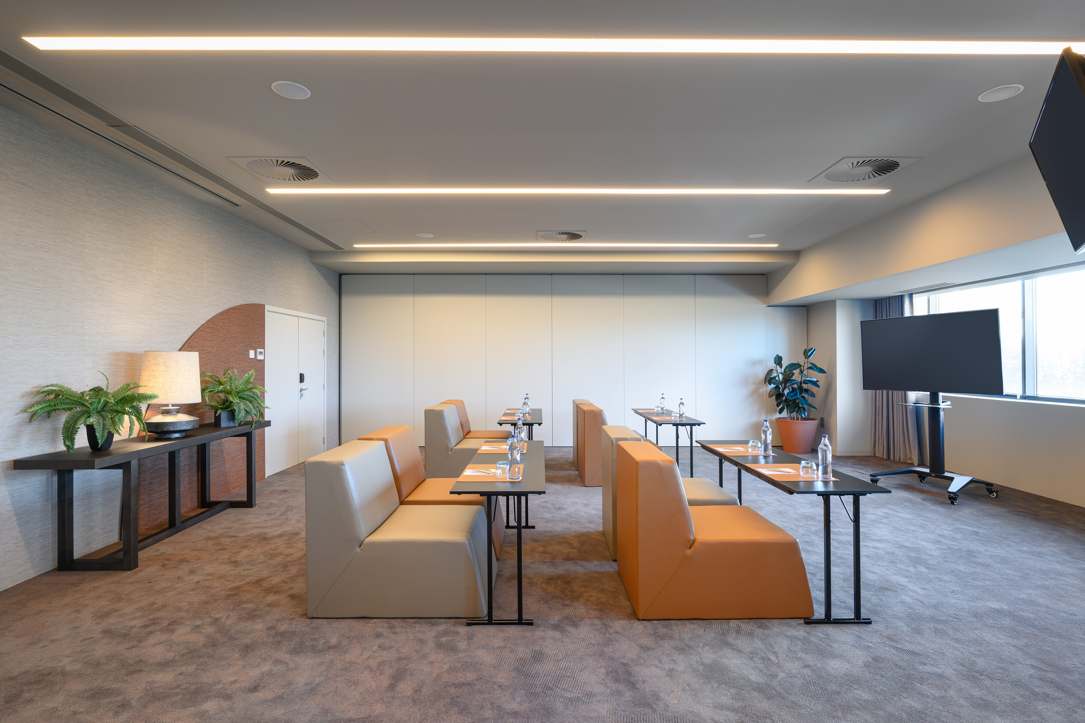 Modern meeting room with modular seating, tables, and presentation display.