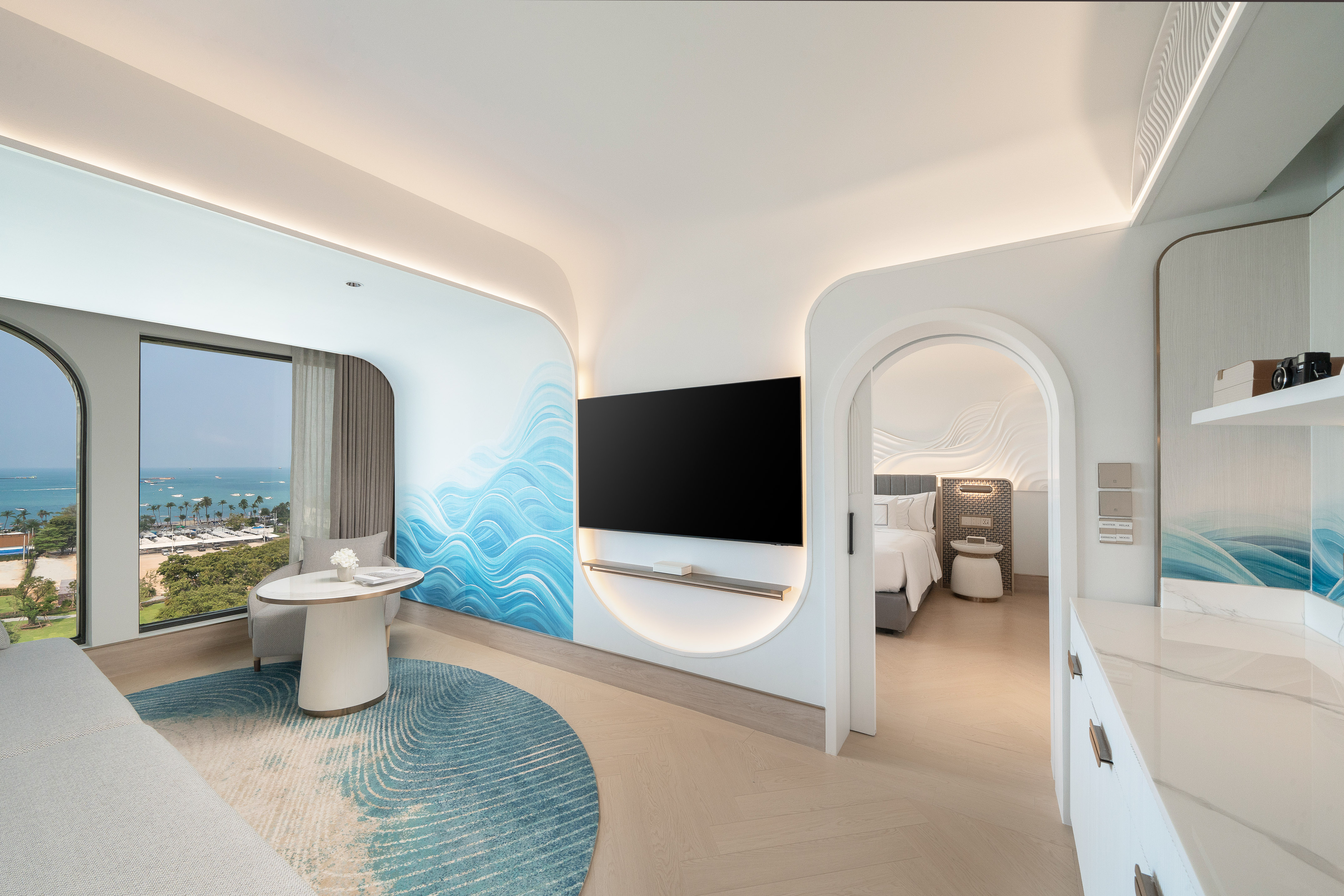 Luxury hotel suite with ocean view, blue wave accent wall, and adjoining bedroom.