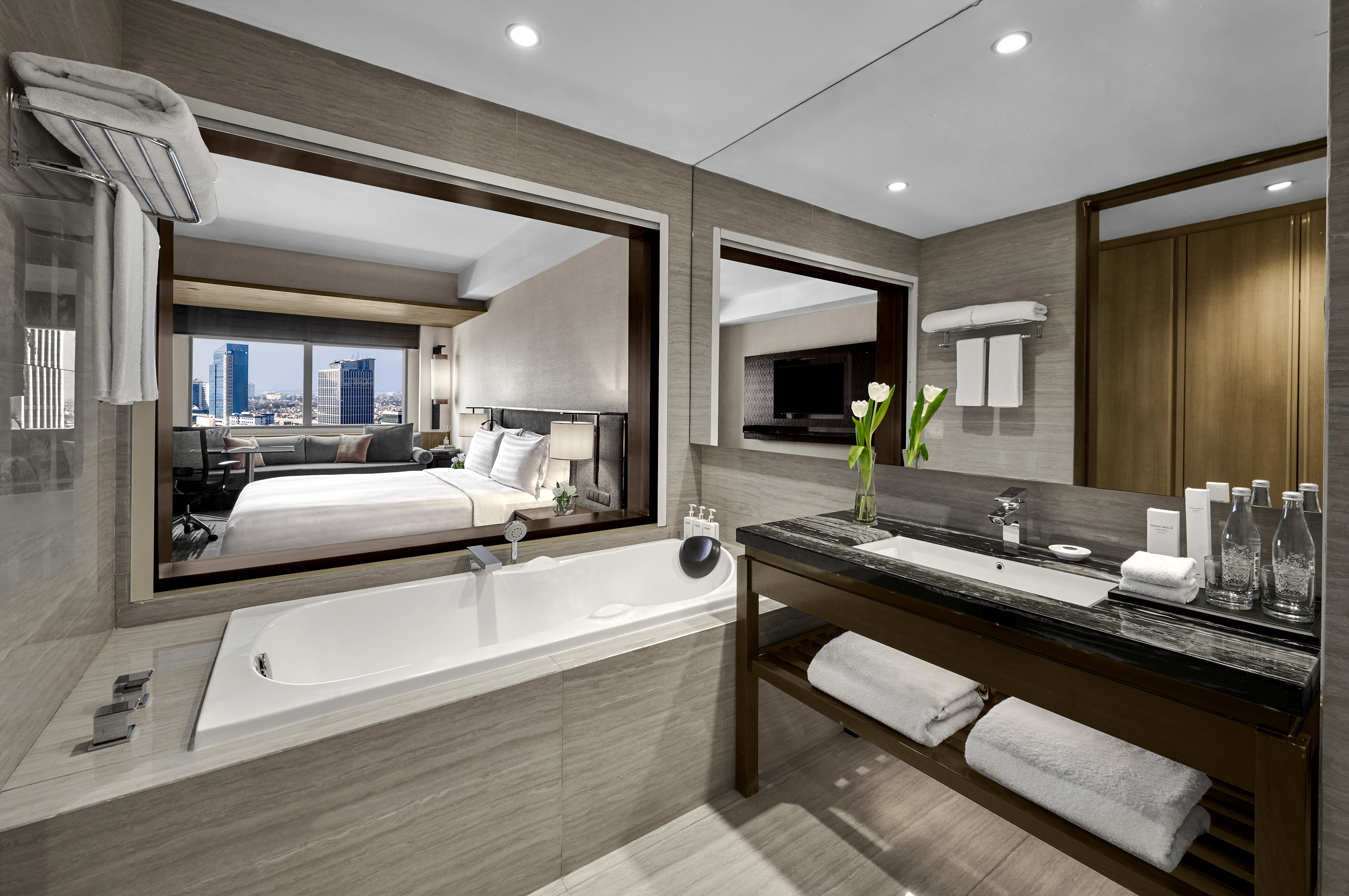 Luxury hotel suite bathroom with bathtub, open concept bedroom, city view.
