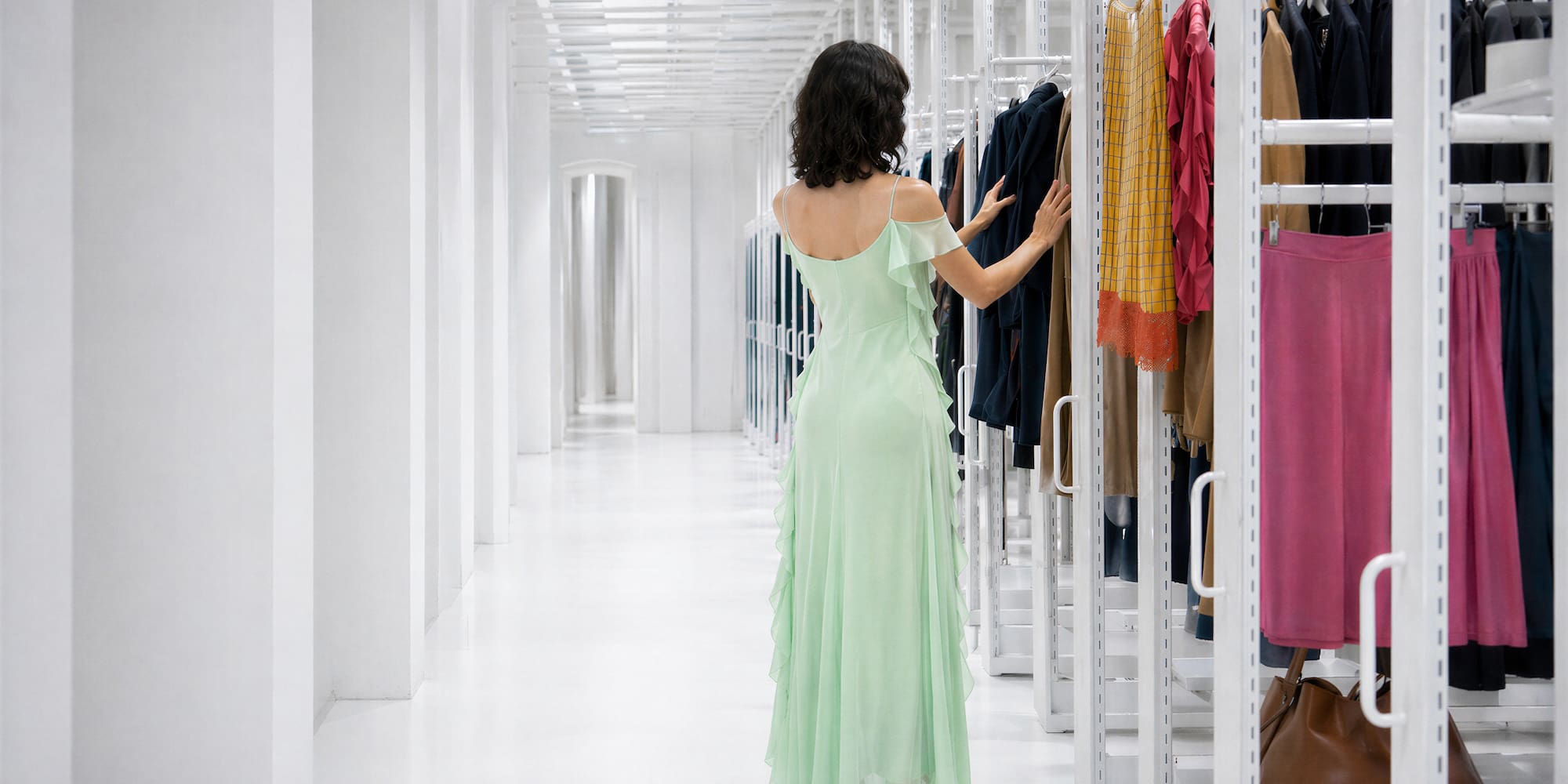 Woman in light green dress browsing clothes in a modern white showroom.