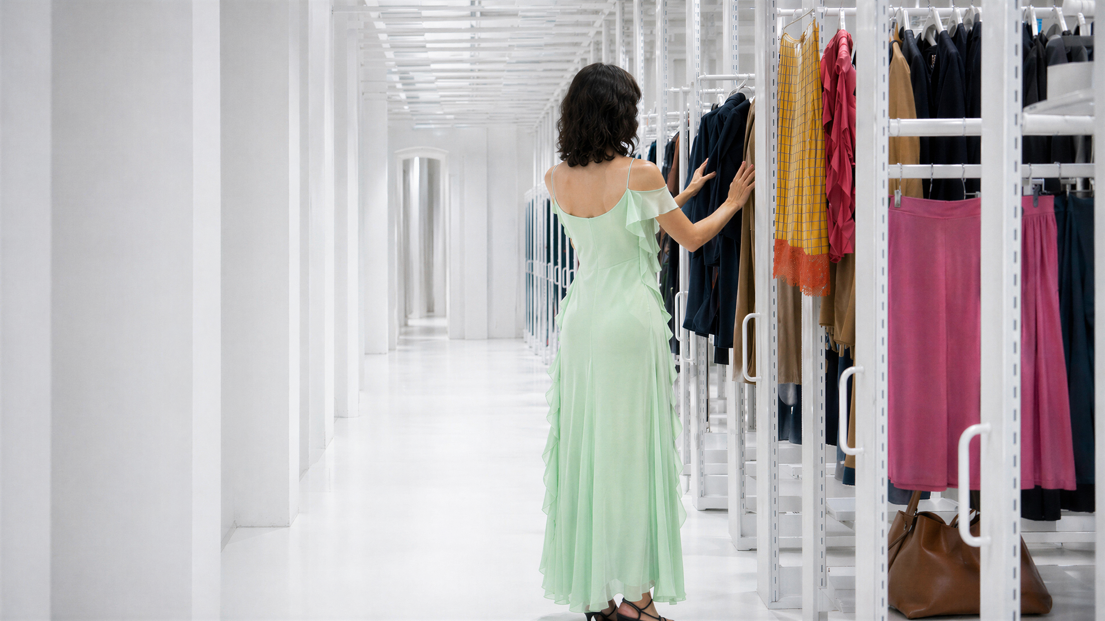 Woman in light green dress browsing clothes in a modern white showroom.