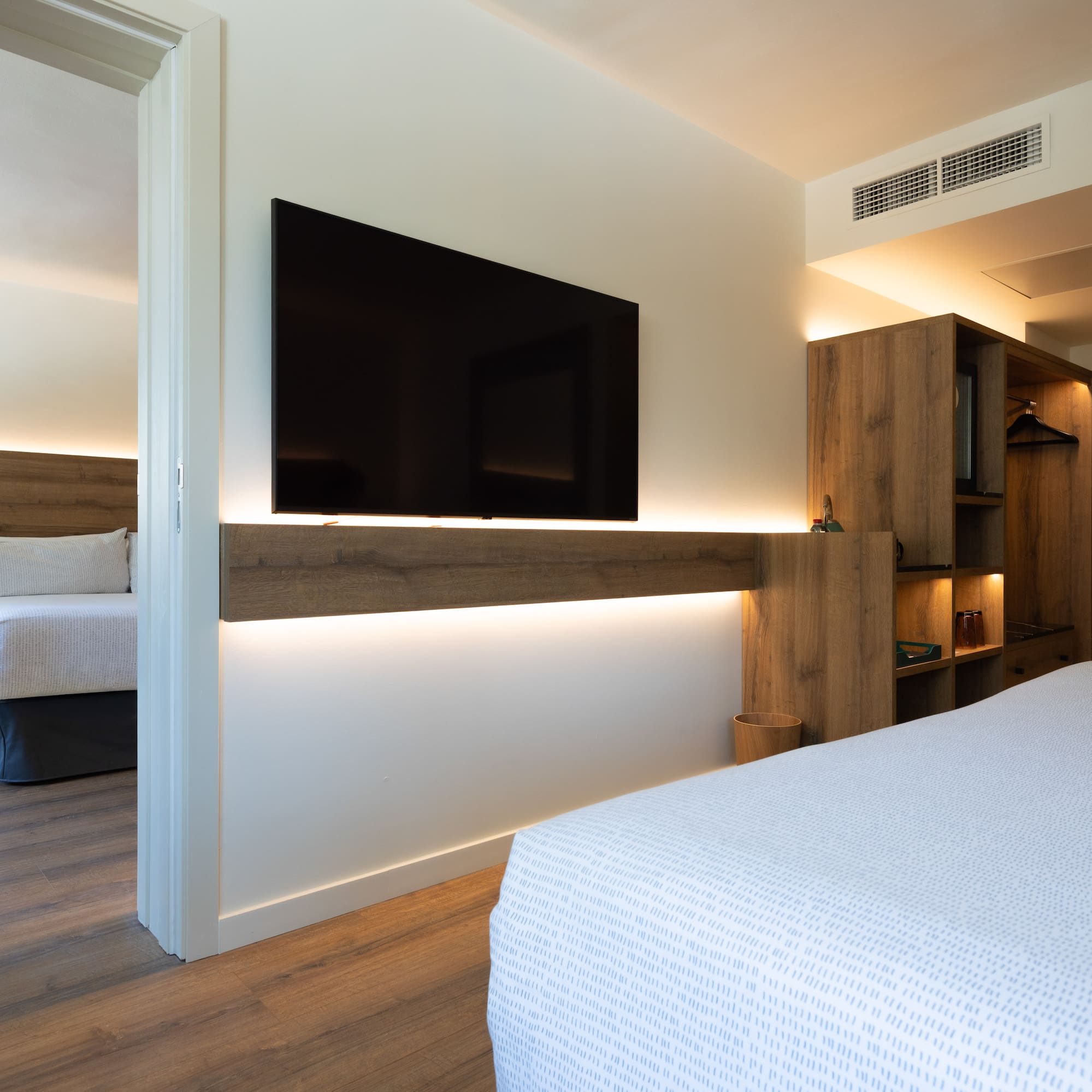Modern hotel suite with flat-screen TV and adjoining bedroom.