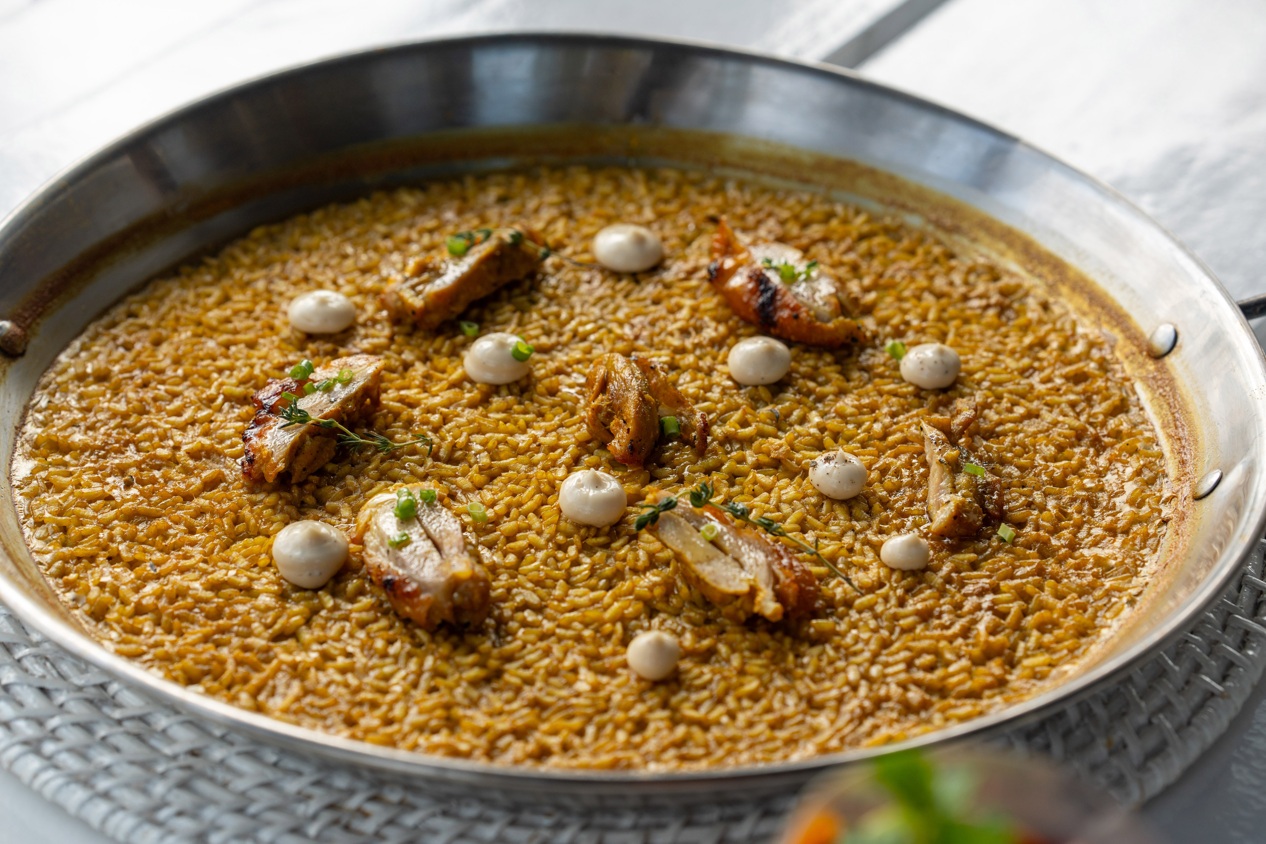 Chicken paella with saffron rice, grilled chicken, aioli, and herbs in a pan.