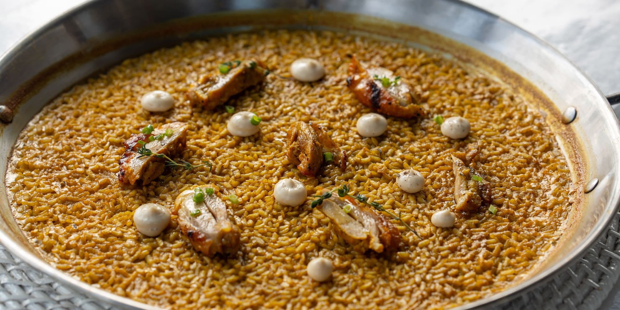 Chicken paella with saffron rice, grilled chicken, aioli, and herbs in a pan.