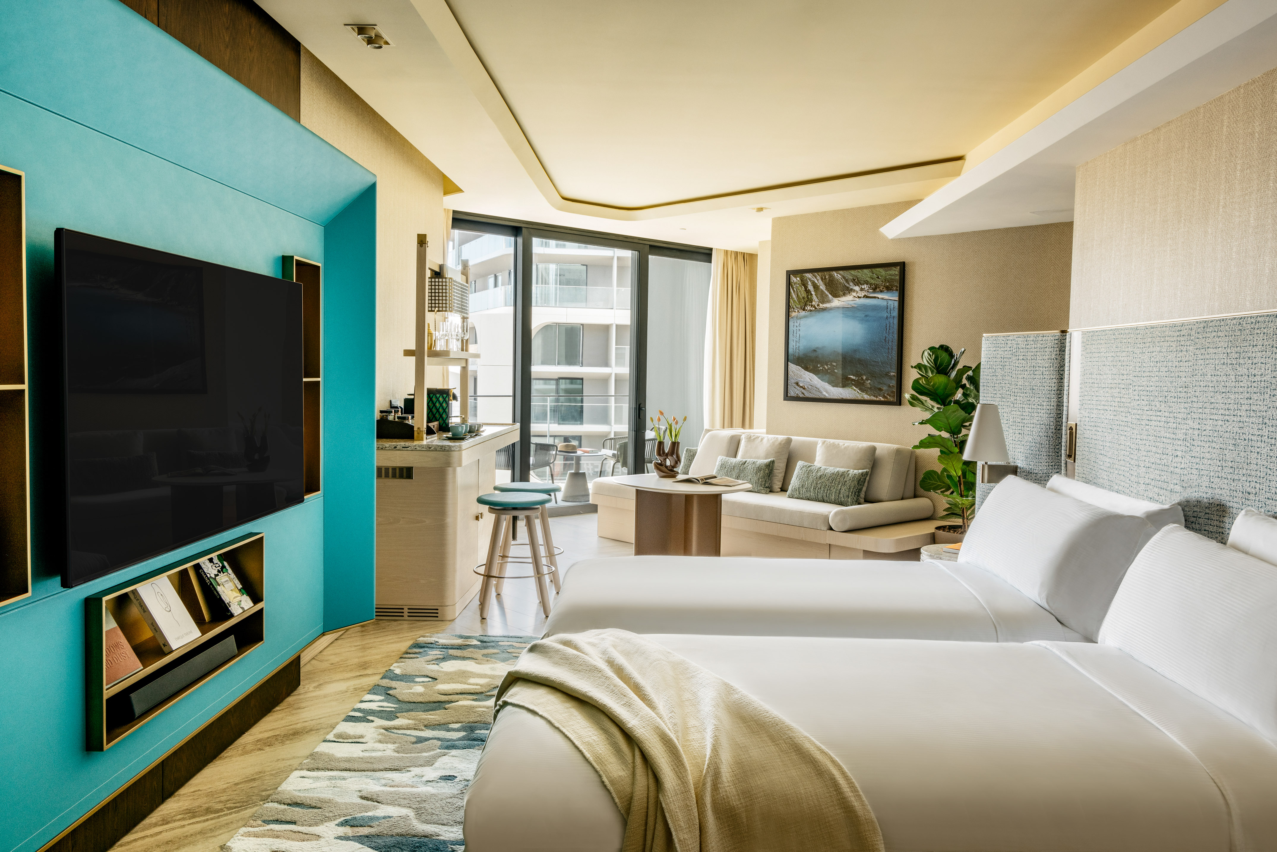 Modern hotel suite with twin beds, living area, kitchenette, and balcony access.