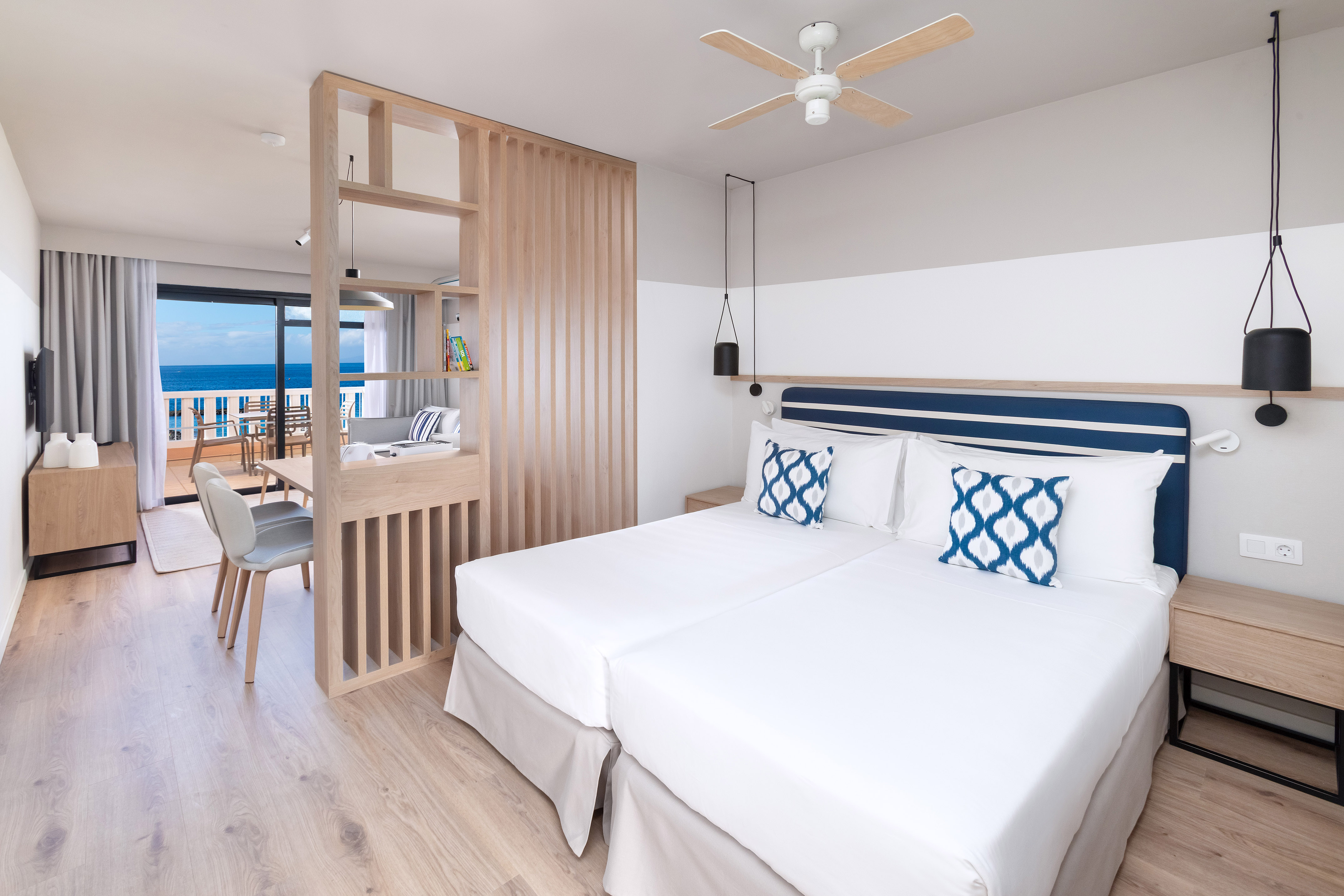 Modern hotel suite with twin beds, ocean view, and wood accents.