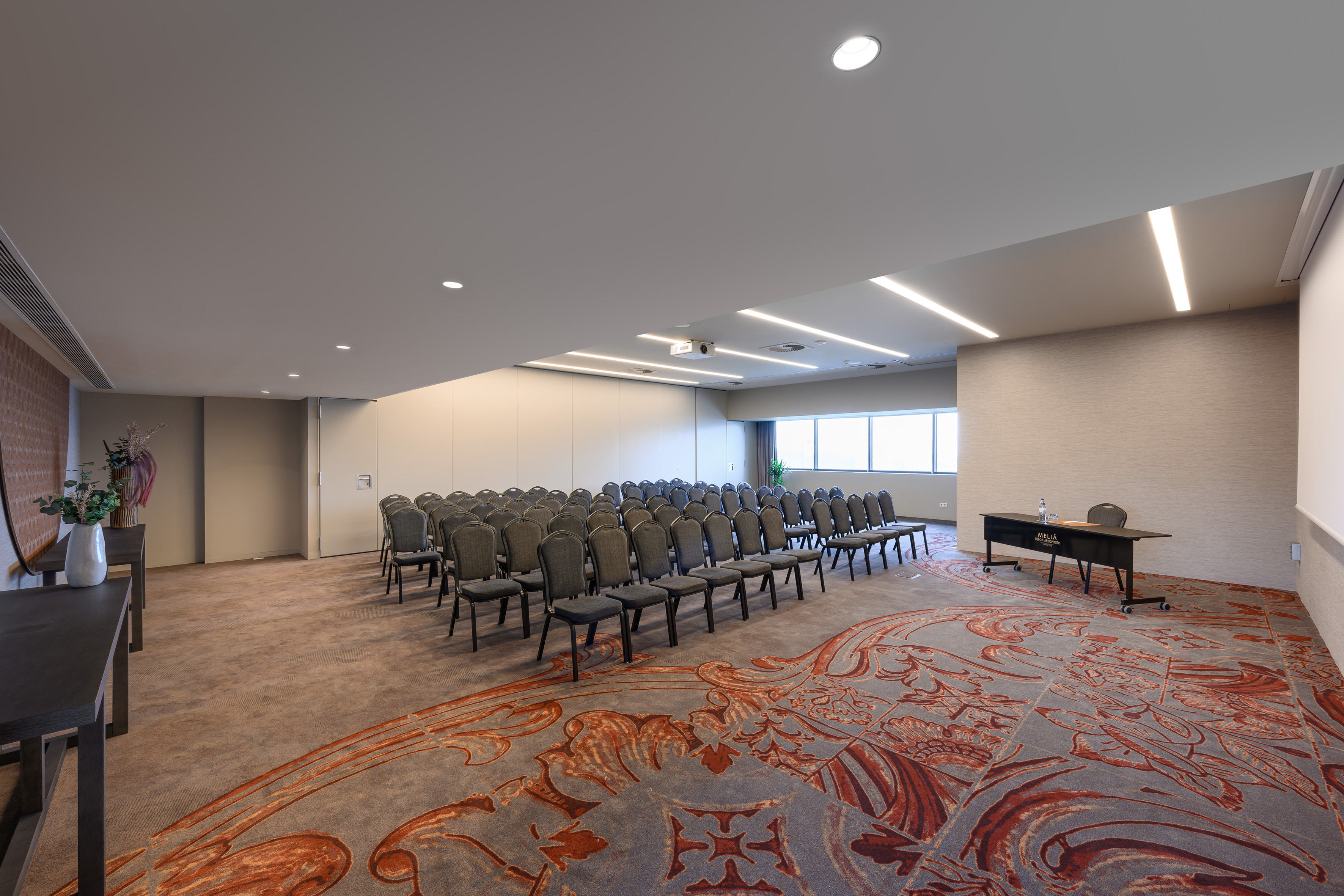 Spacious conference room with theater seating, projector, and ornate carpet.