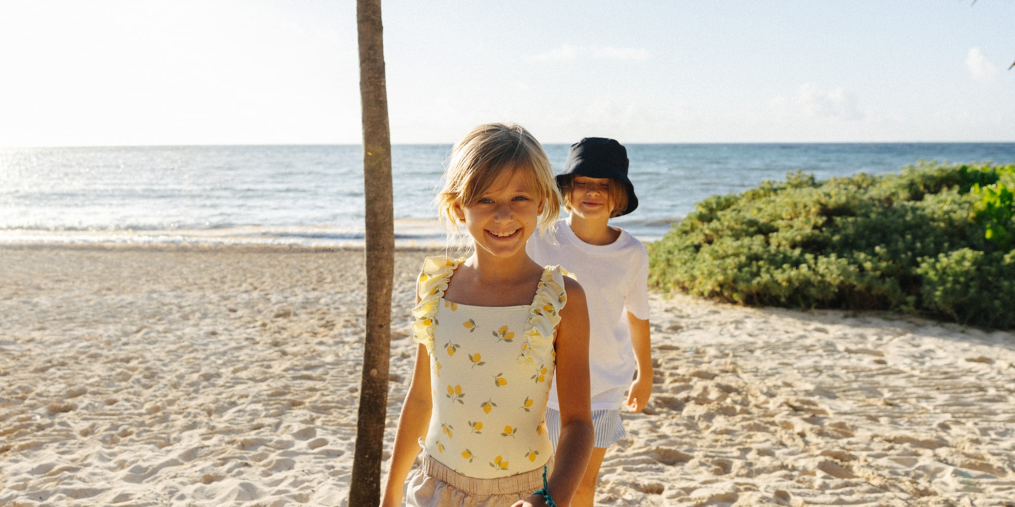 Smiling girl in lemon swimsuit and boy on sunny beach with ocean.
