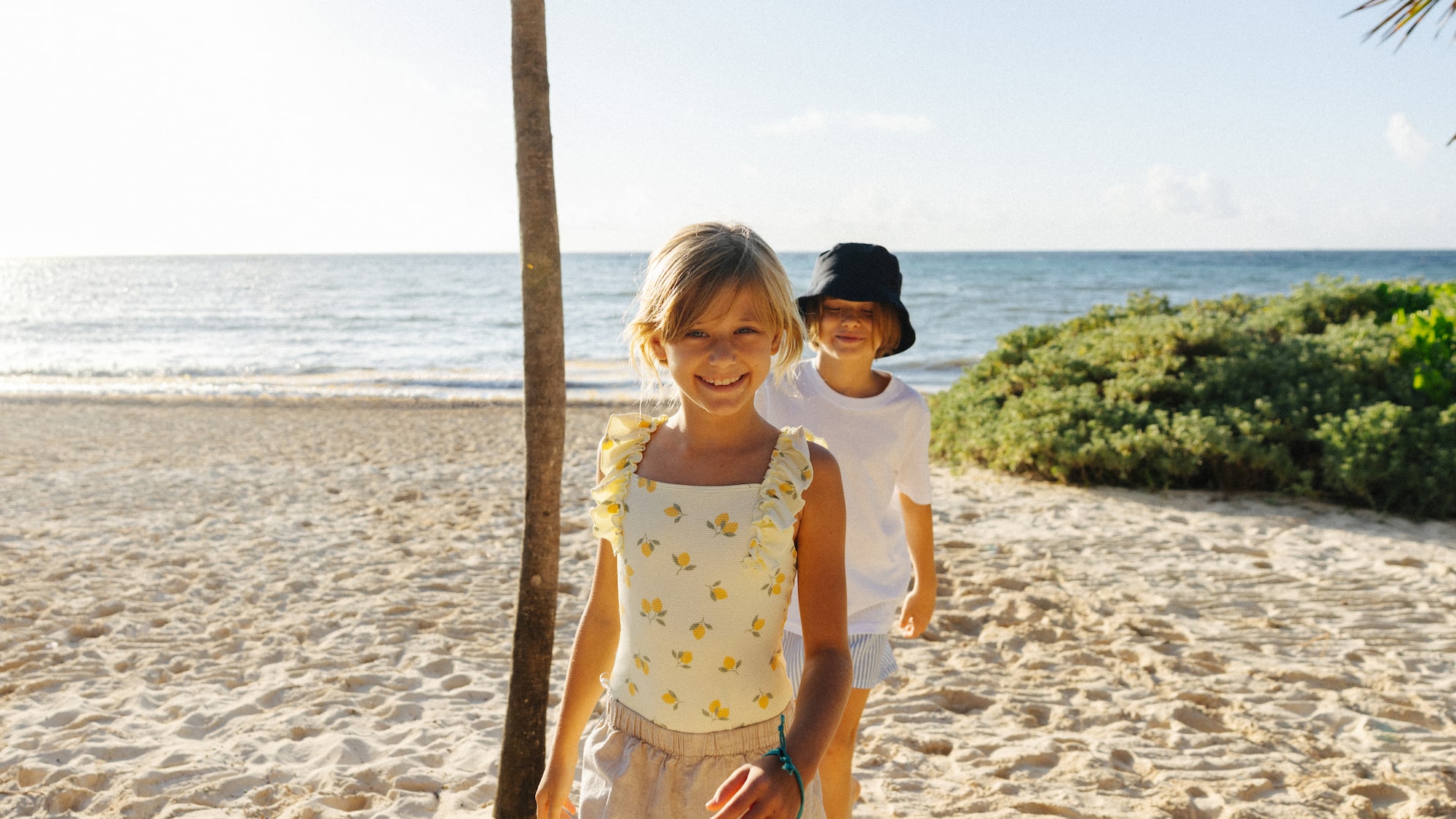 Smiling girl in lemon swimsuit and boy on sunny beach with ocean.