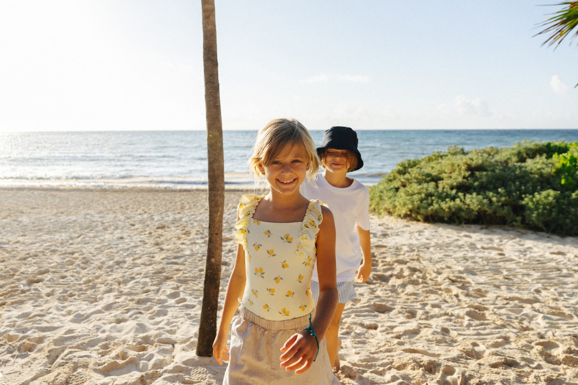 Smiling girl in lemon swimsuit and boy on sunny beach with ocean.