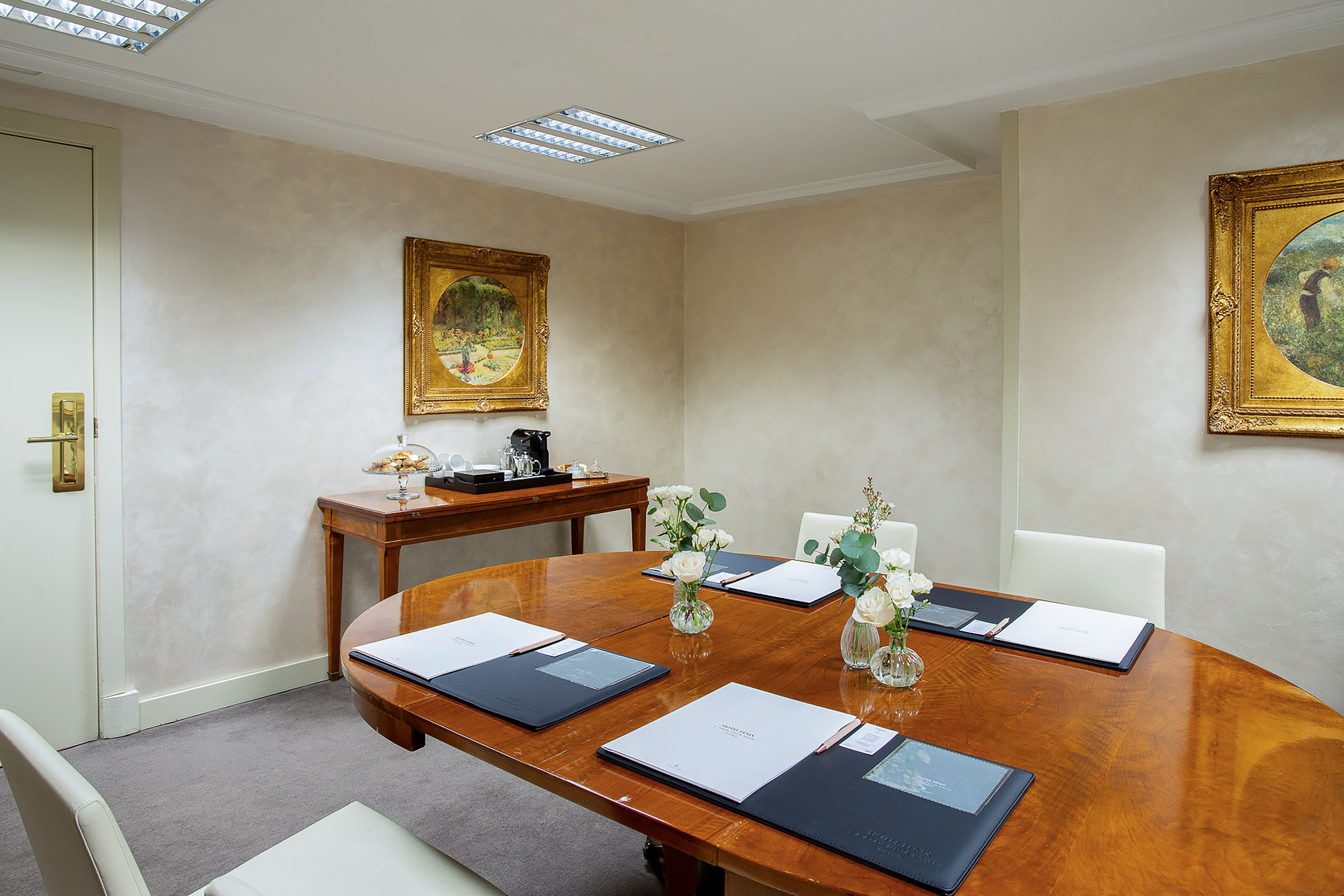 Hotel meeting room with oval wooden table, chairs, and coffee station.